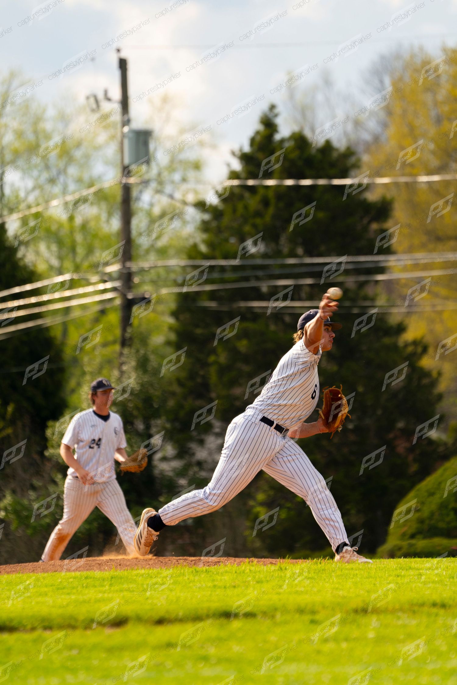 Baseball pitcher in pinstripe uniform delivering a pitch with teammate visible in background.