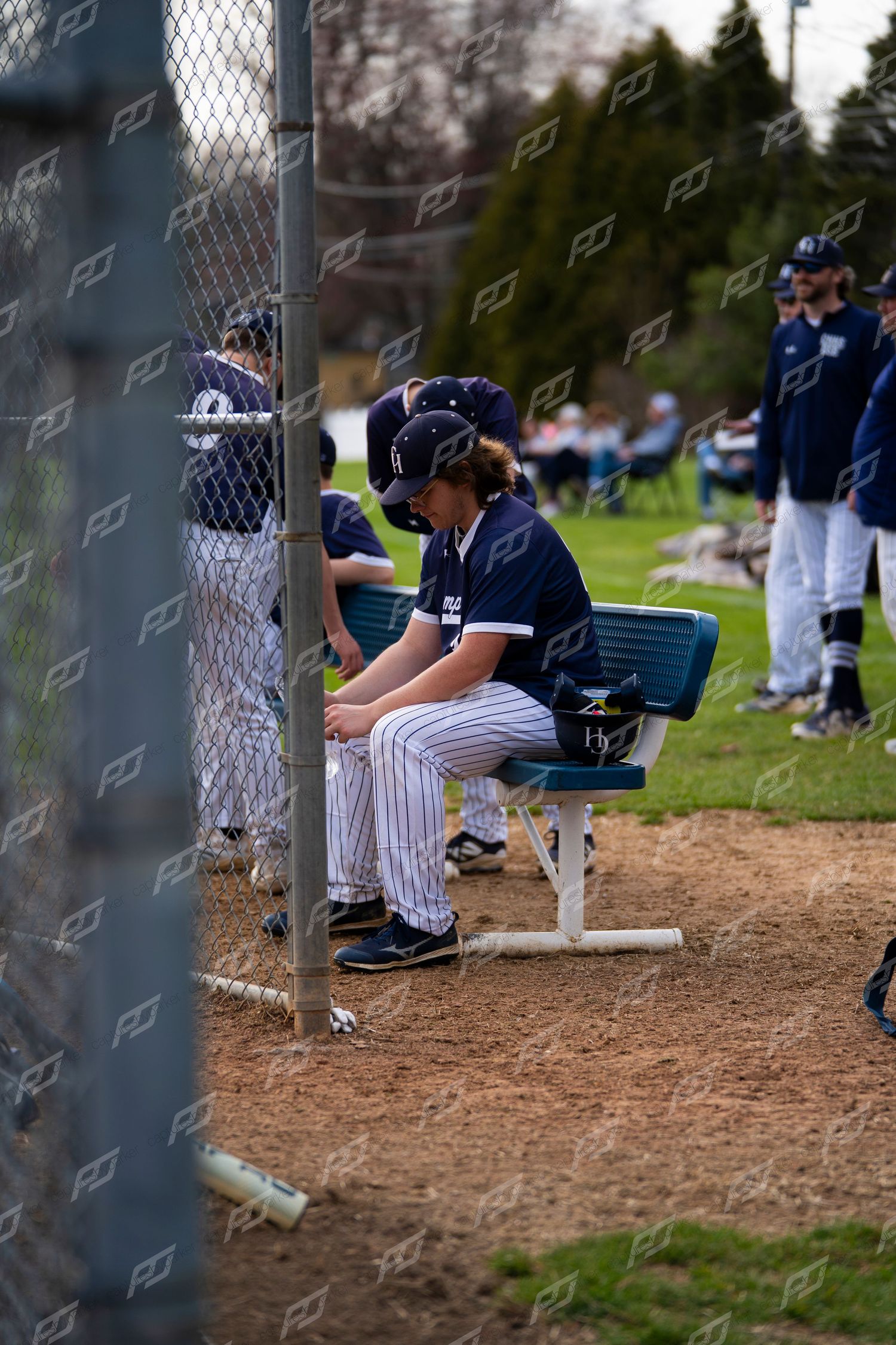 Baseball player in navy pinstripe uniform sitting pensively in the dugout during a youth league game.