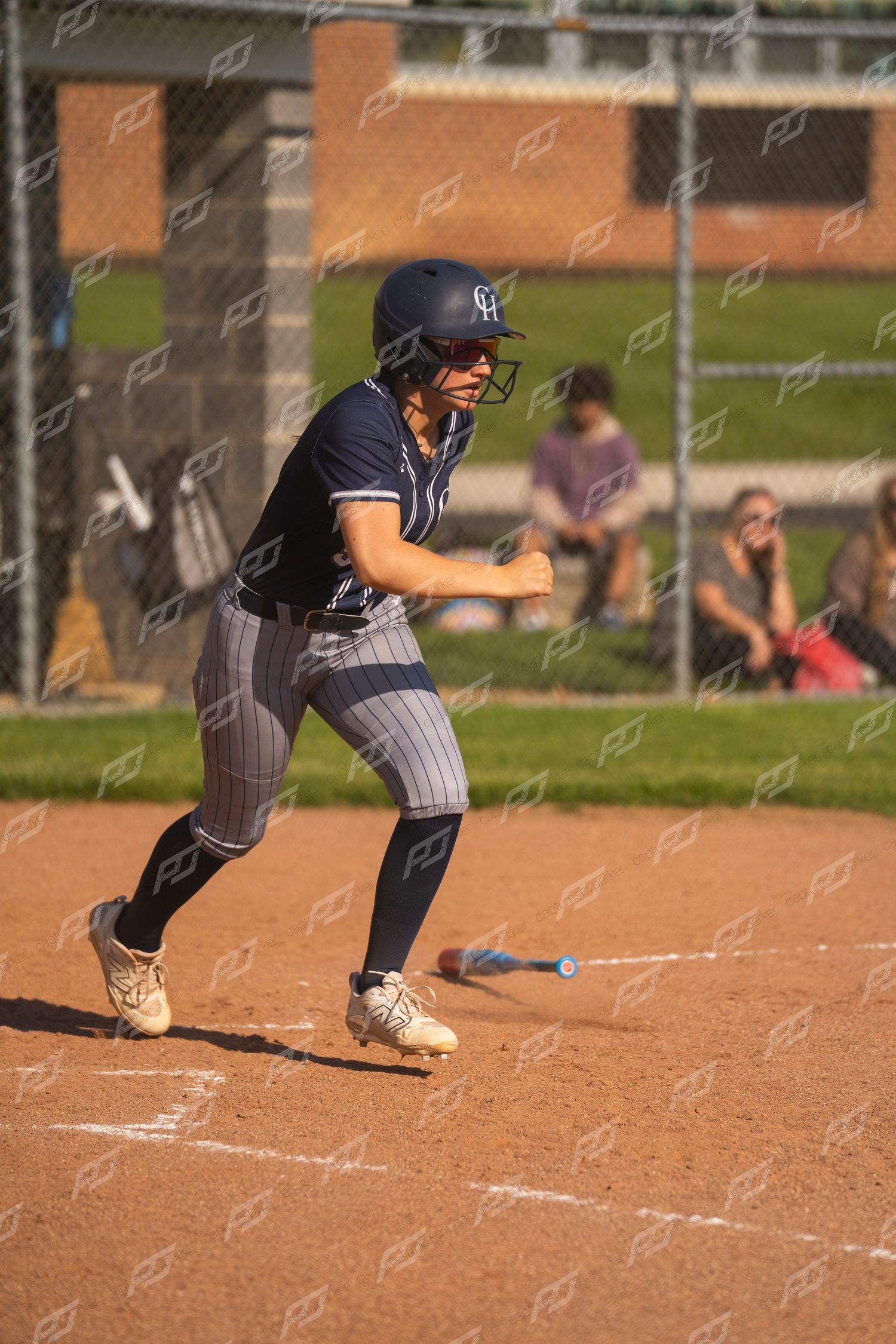 Female softball player in navy uniform sprints from home plate after hitting the ball.
