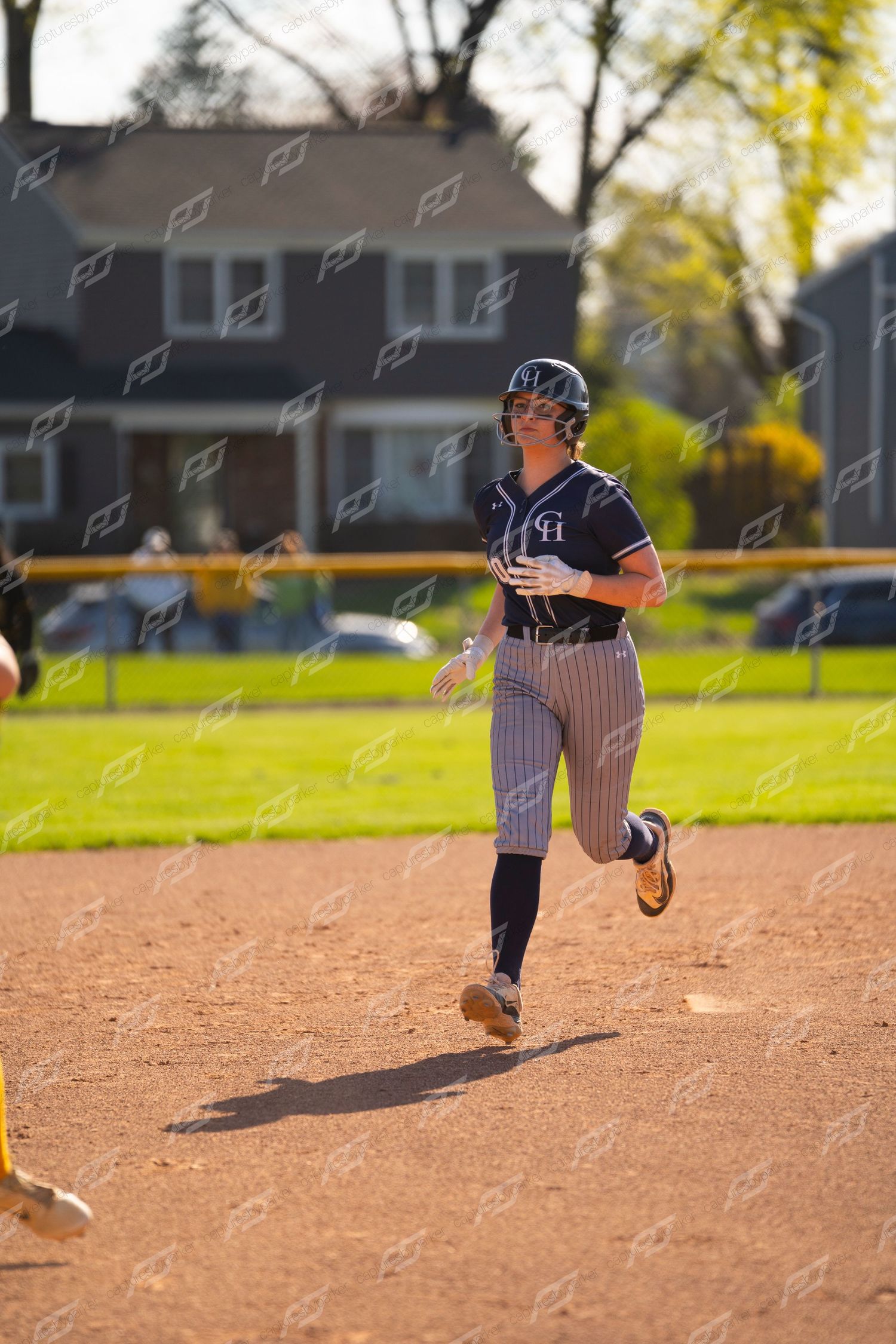 Female softball player in navy pinstripe uniform running bases on dirt infield during sunny game.