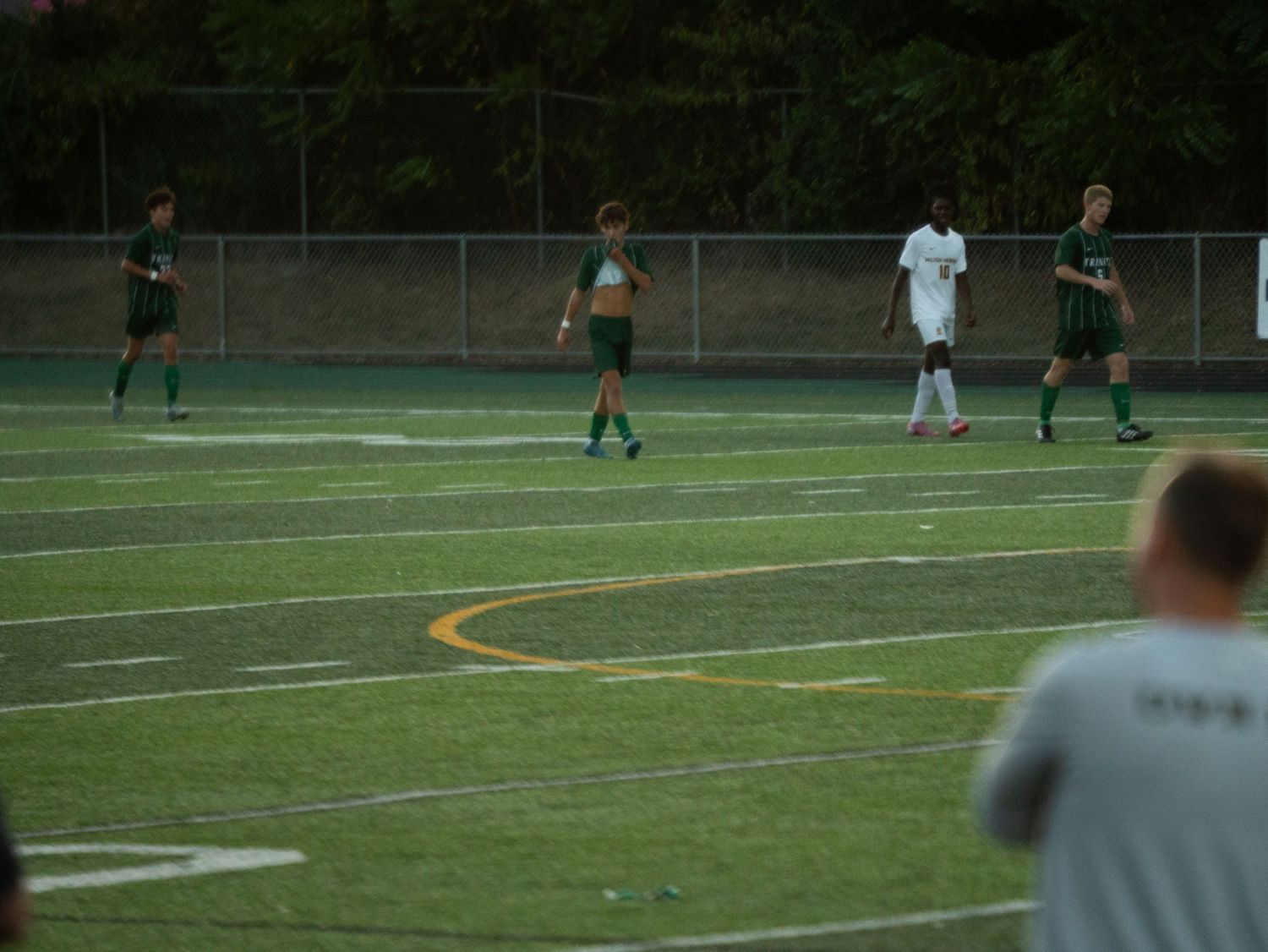 Green-uniformed soccer players compete on an artificial turf field during a youth soccer match.