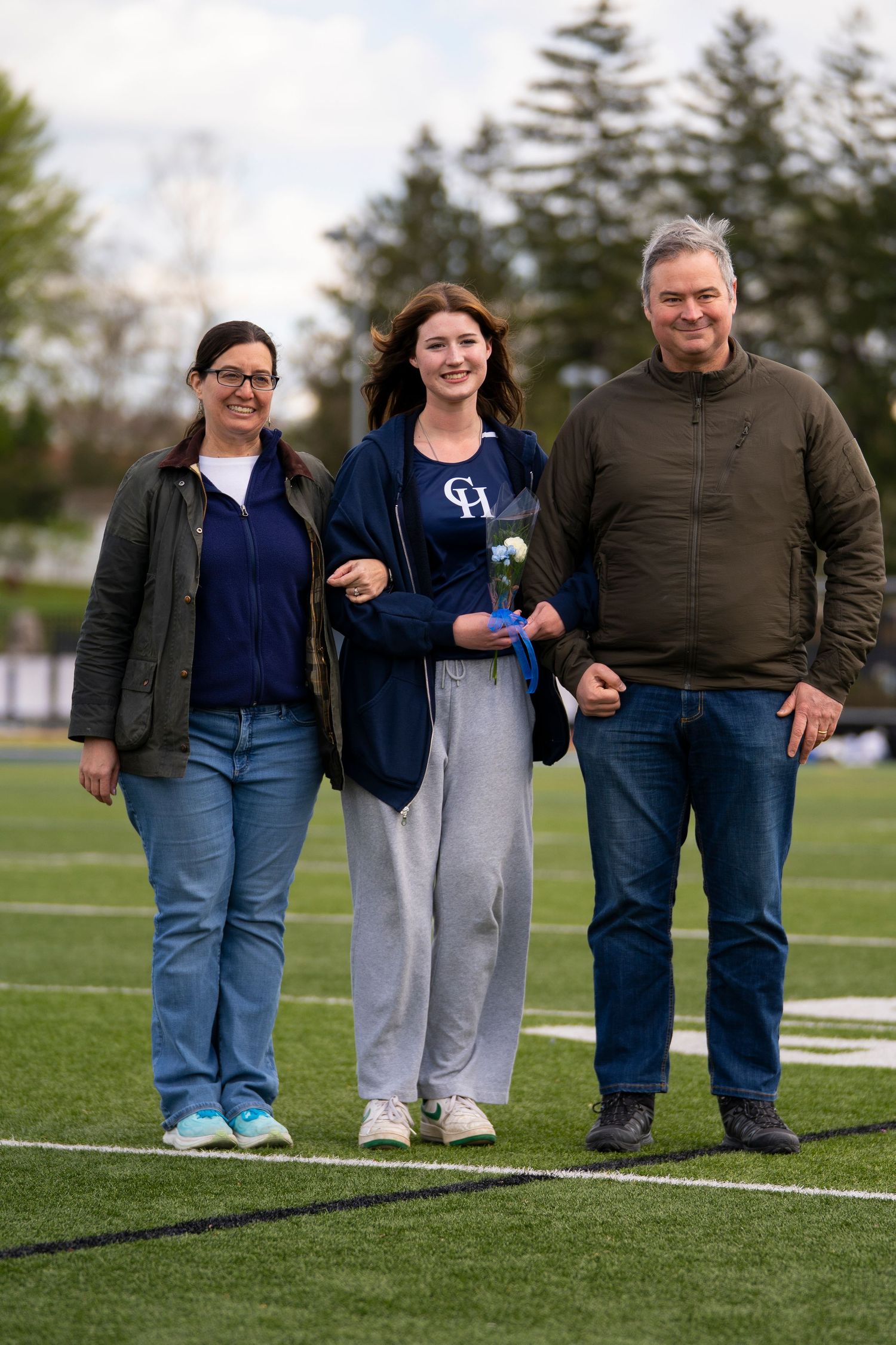 A student athlete poses with two family members on a football field during senior day.