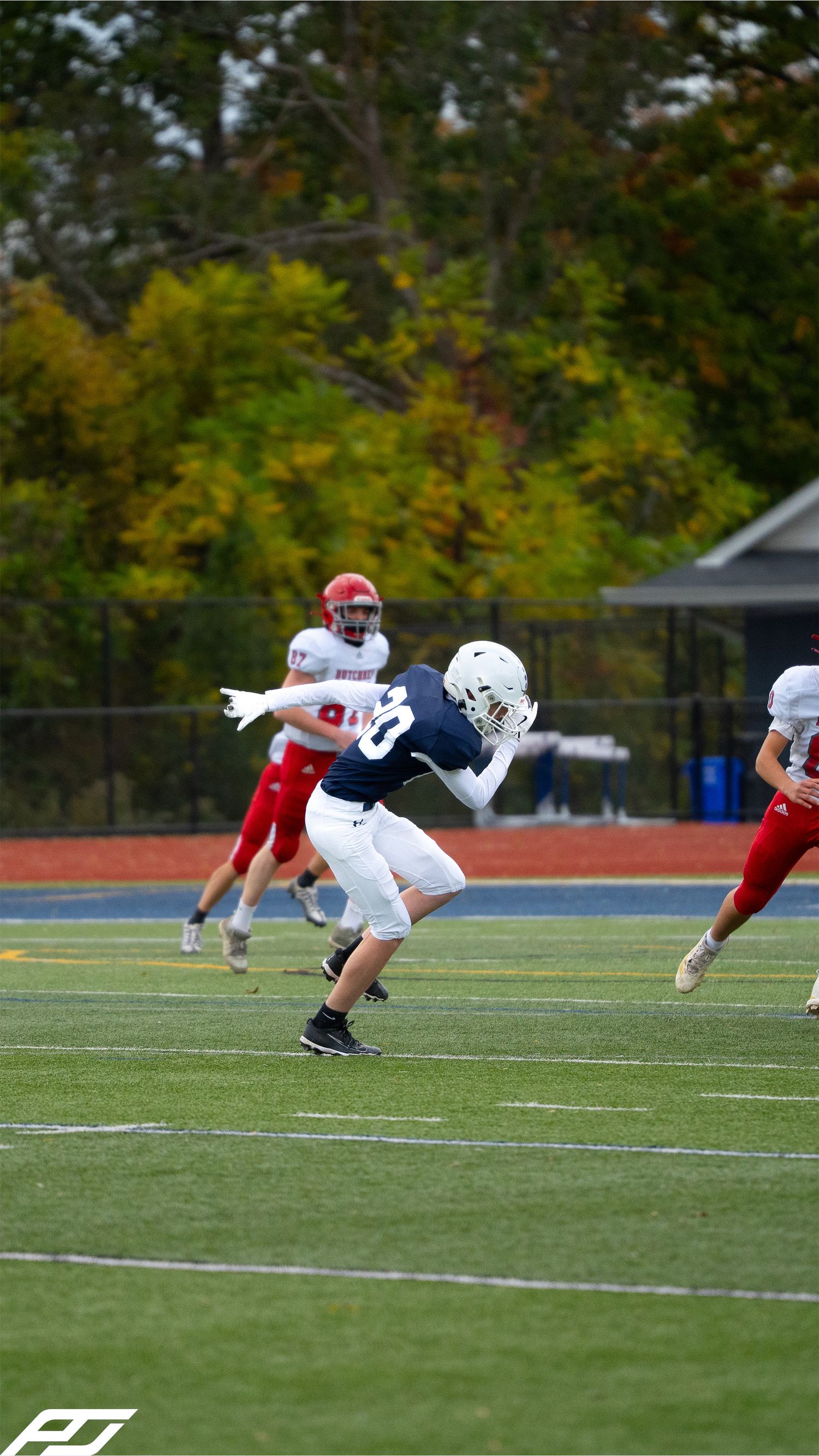 Youth football player in navy uniform number 10 runs a route on turf against red-jersyed defenders.