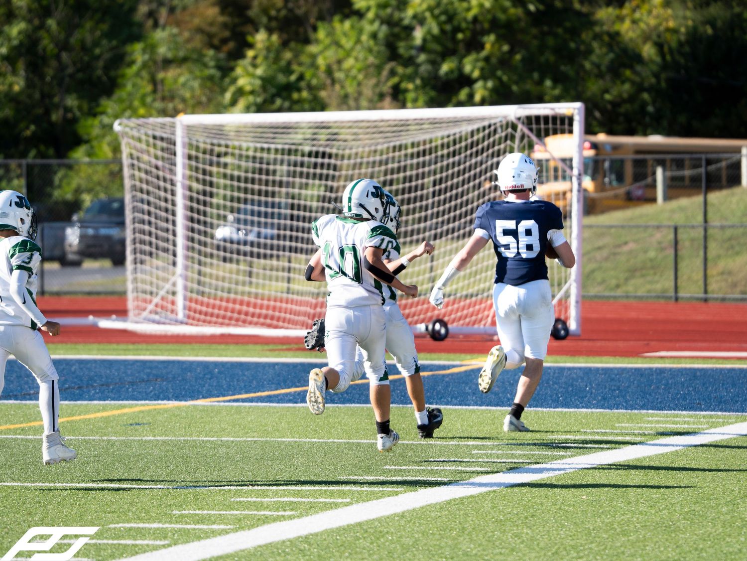 Football player in green uniform runs with the ball as navy-uniformed player 58 gives chase near goal post.