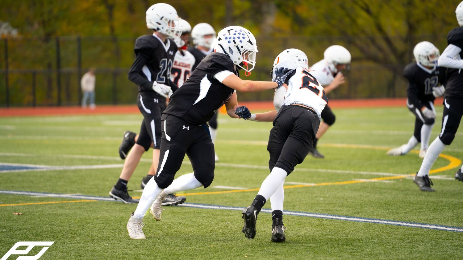 Youth football player in black uniform runs with the ball during a game.