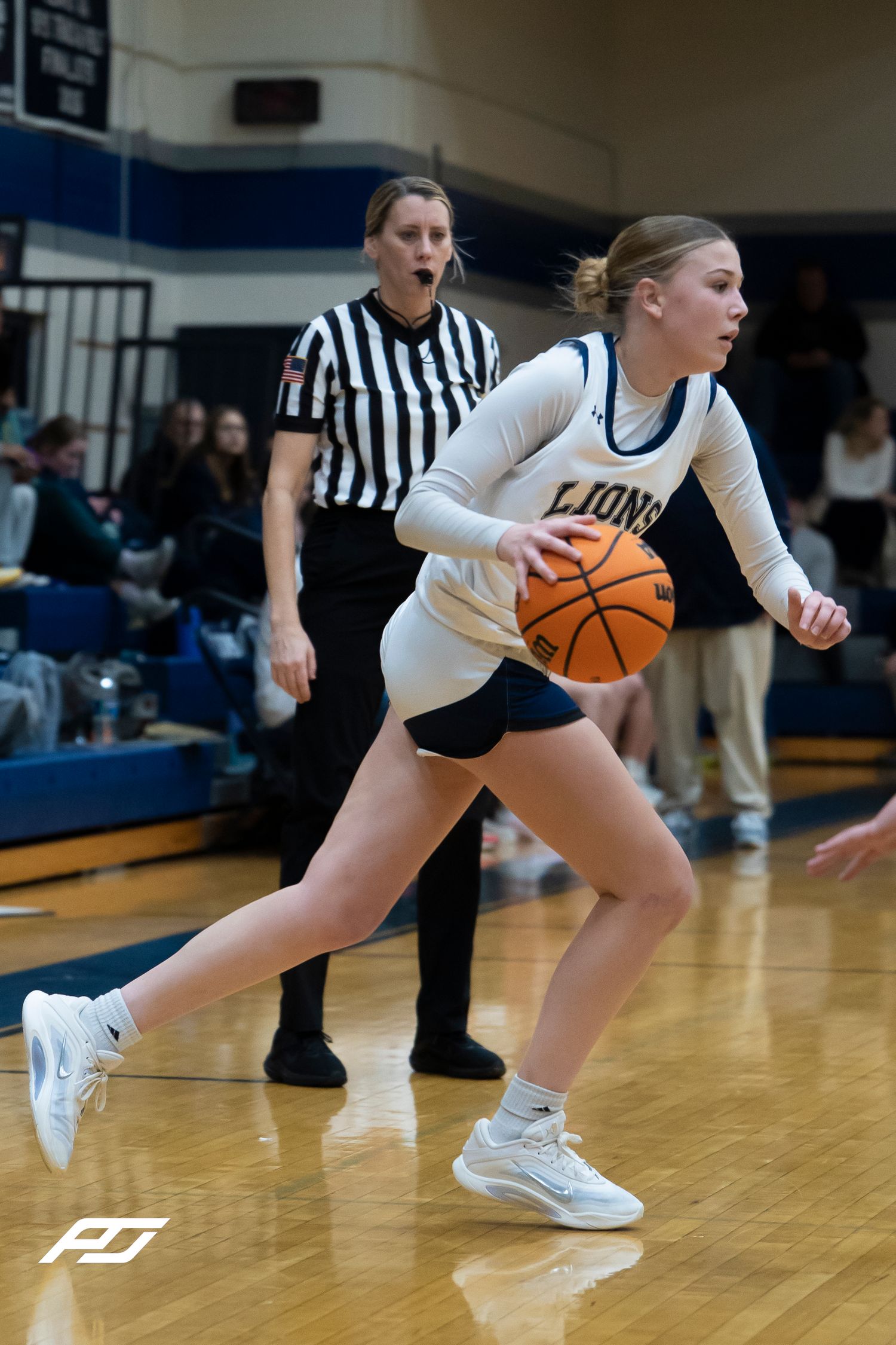 Lions female basketball player drives with ball as referee watches during high school basketball game.