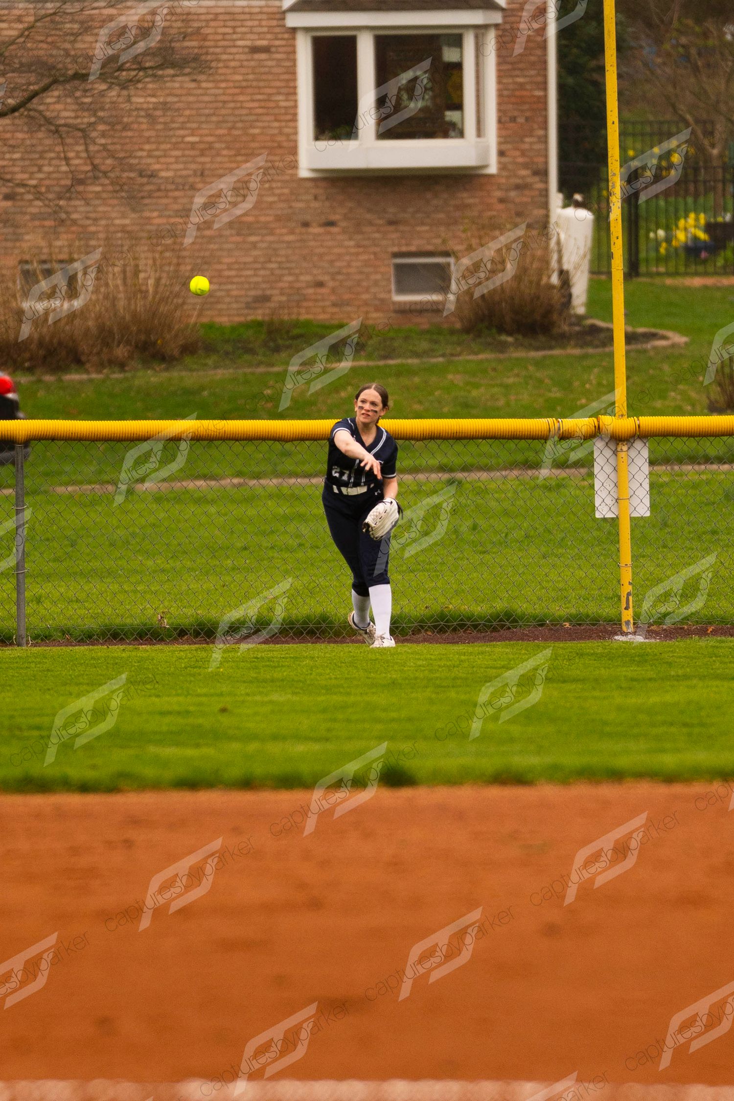 Female softball outfielder in navy uniform throws ball from deep right field.