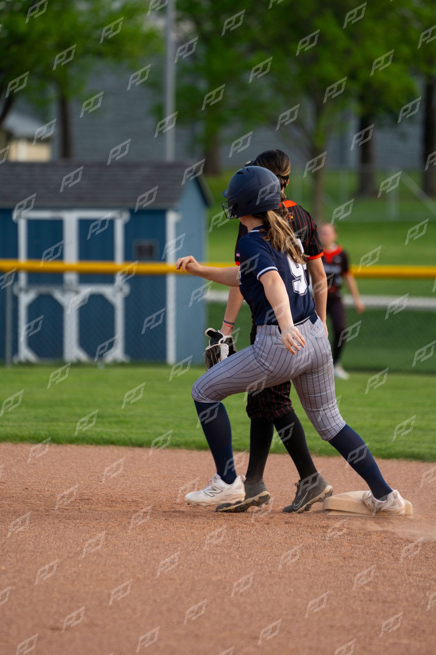 Female softball player in navy uniform reaches base during competitive game.