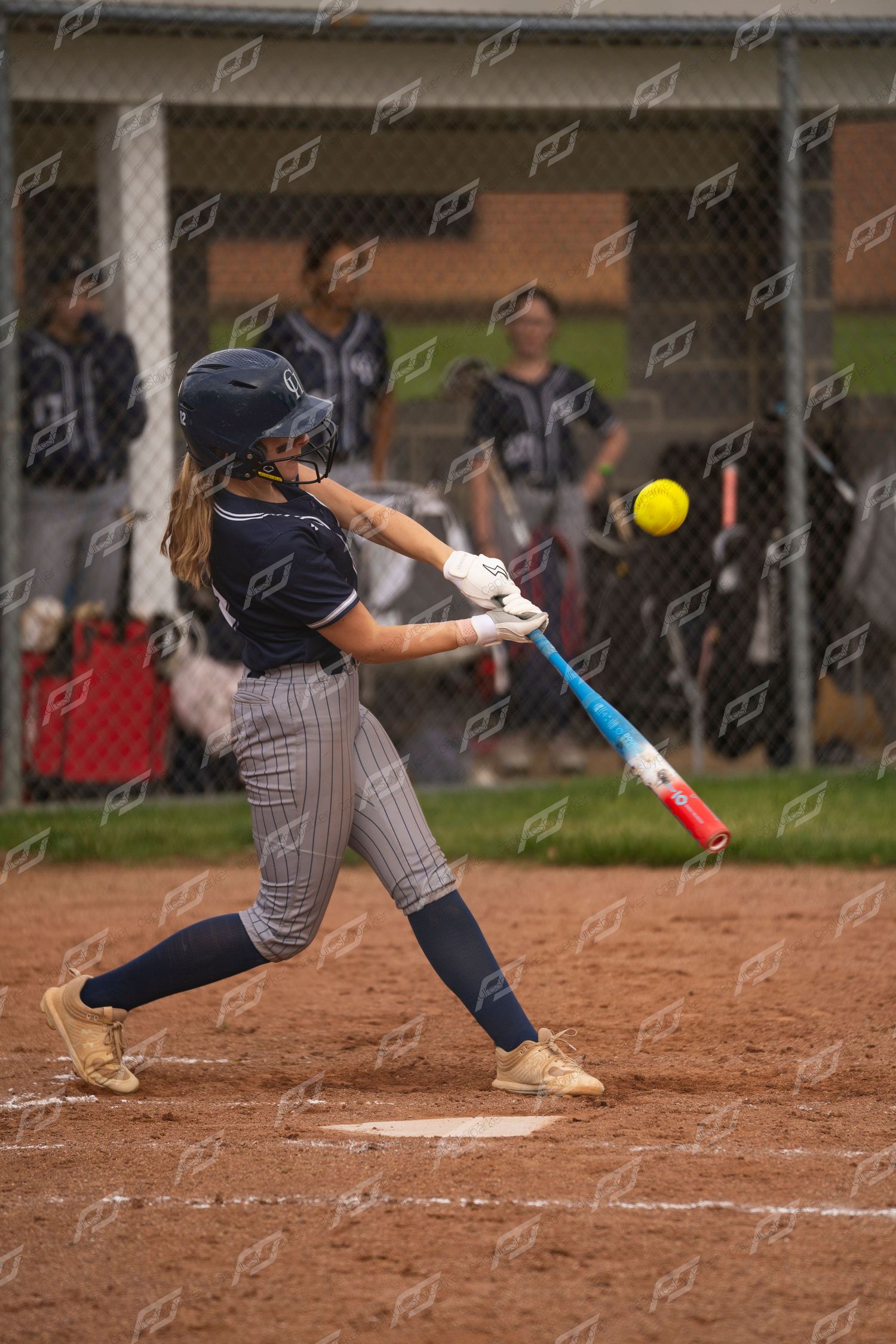 Female softball player swings at a yellow softball with a colorful bat during a game.