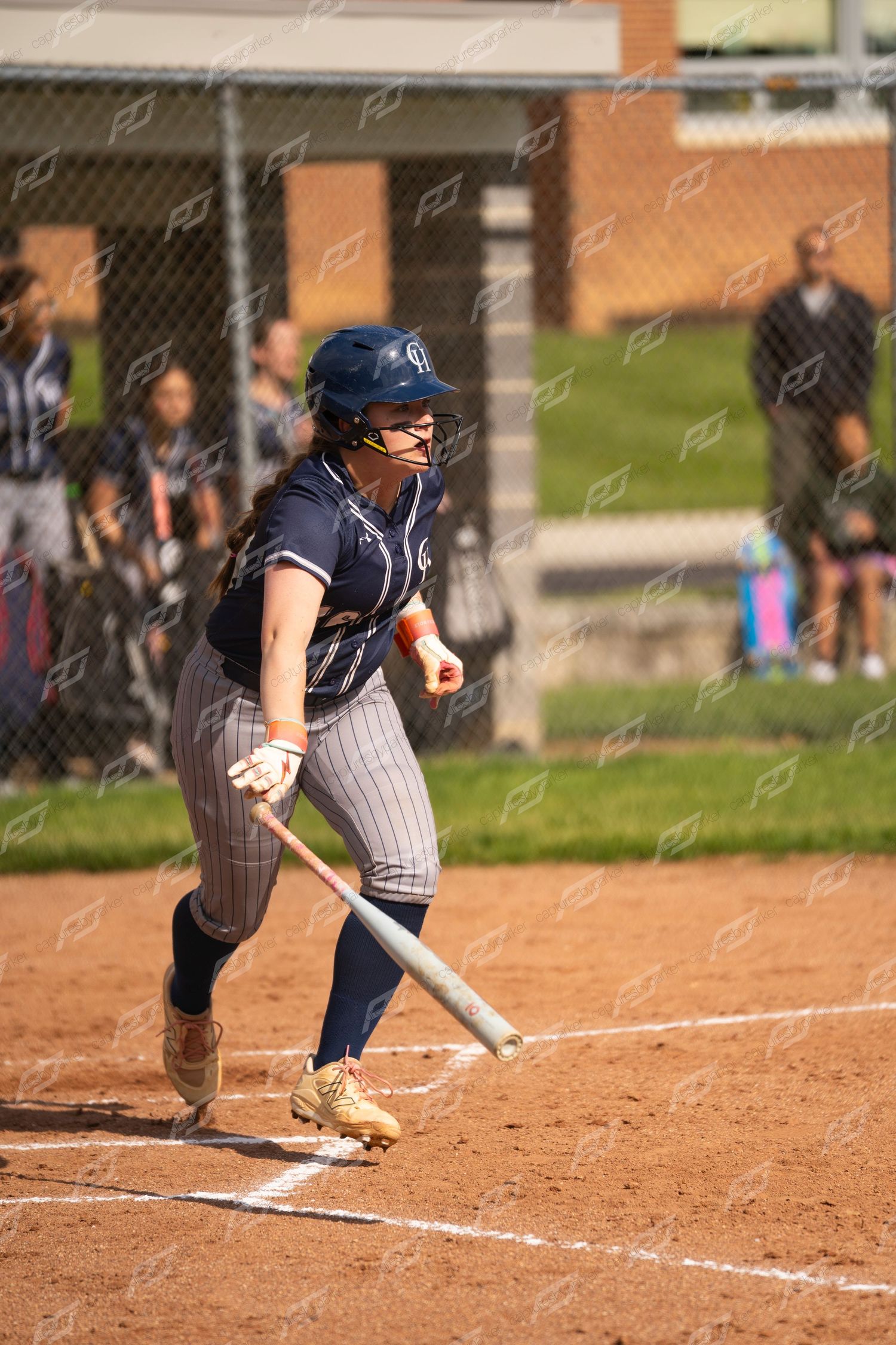 Female softball player in navy pinstripe uniform completes batting stance during outdoor game.