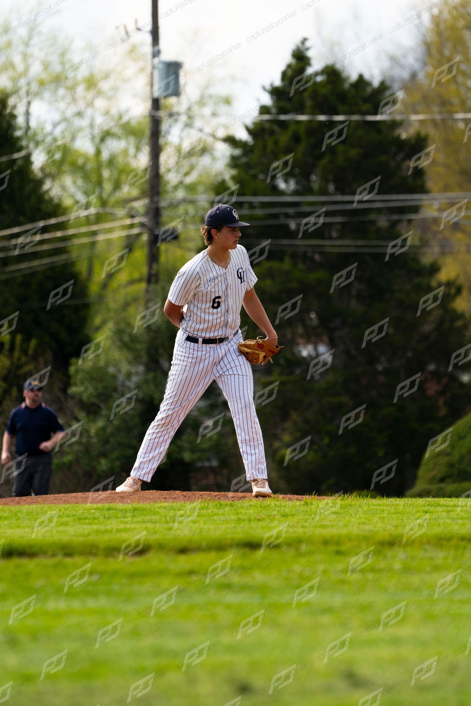 Youth baseball pitcher #6 in white pinstripe uniform standing on the mound ready to pitch.
