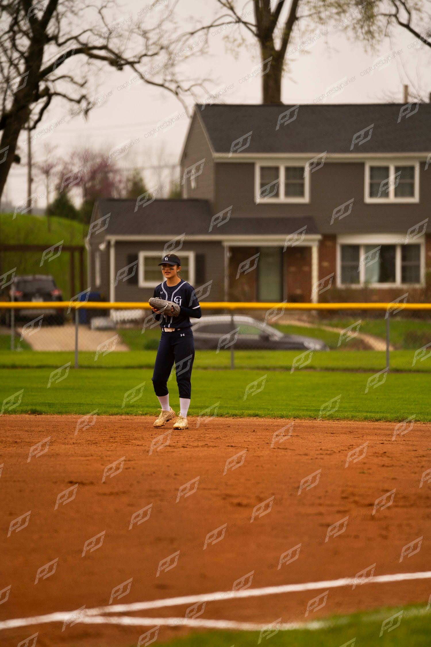 Softball player in navy uniform standing at base holding ball on red clay infield during game.