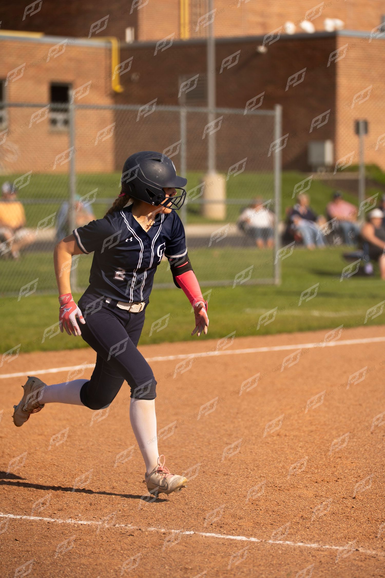 Female softball player in navy uniform runs bases during a sunny outdoor game.