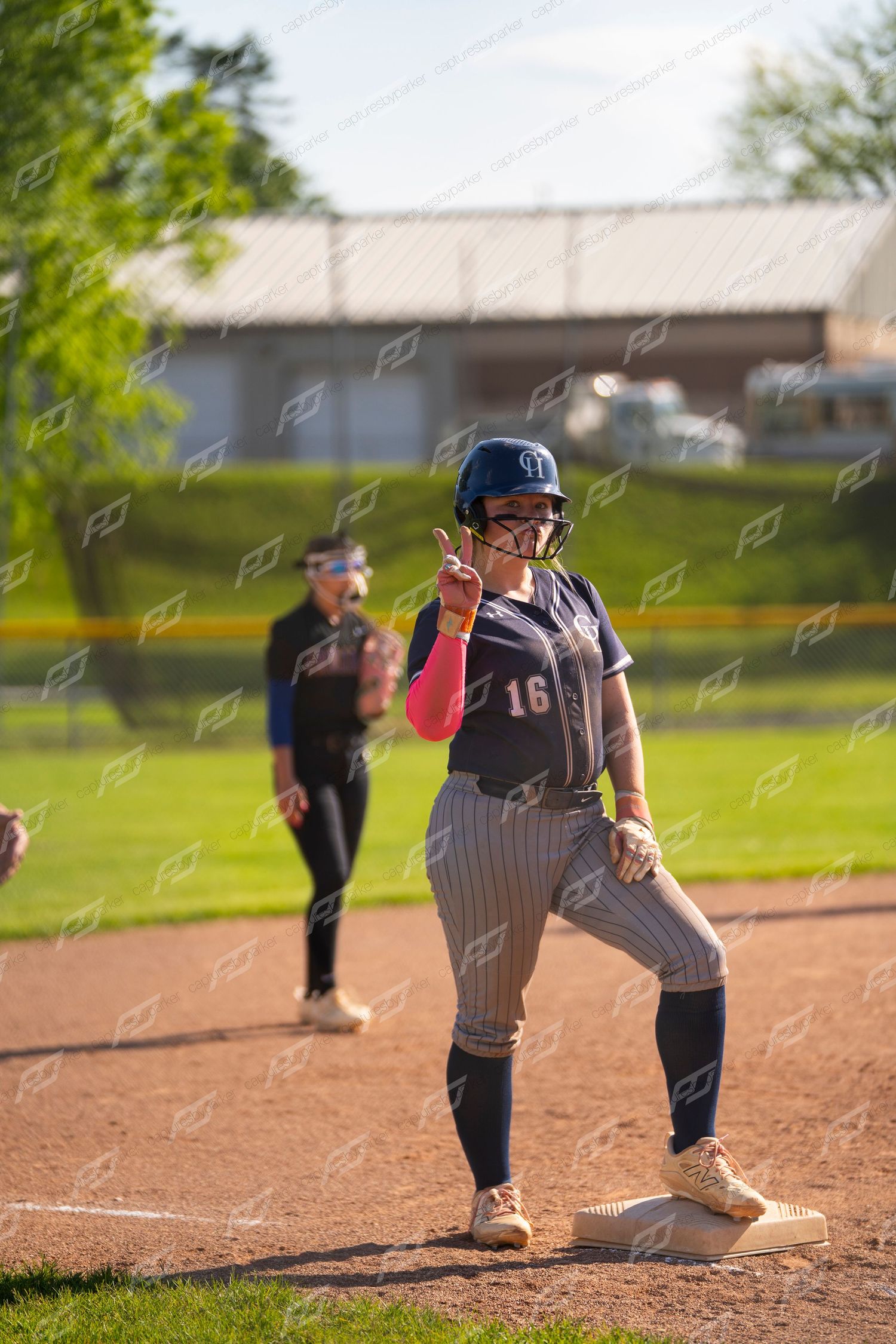 Female softball player number 16 standing on base giving a peace sign during a game.