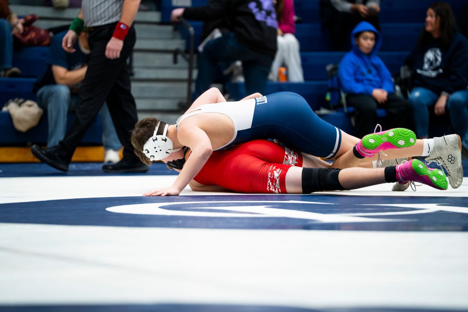 Blue-uniformed wrestler pins red-singlet opponent to the mat during a competitive high school wrestling match.