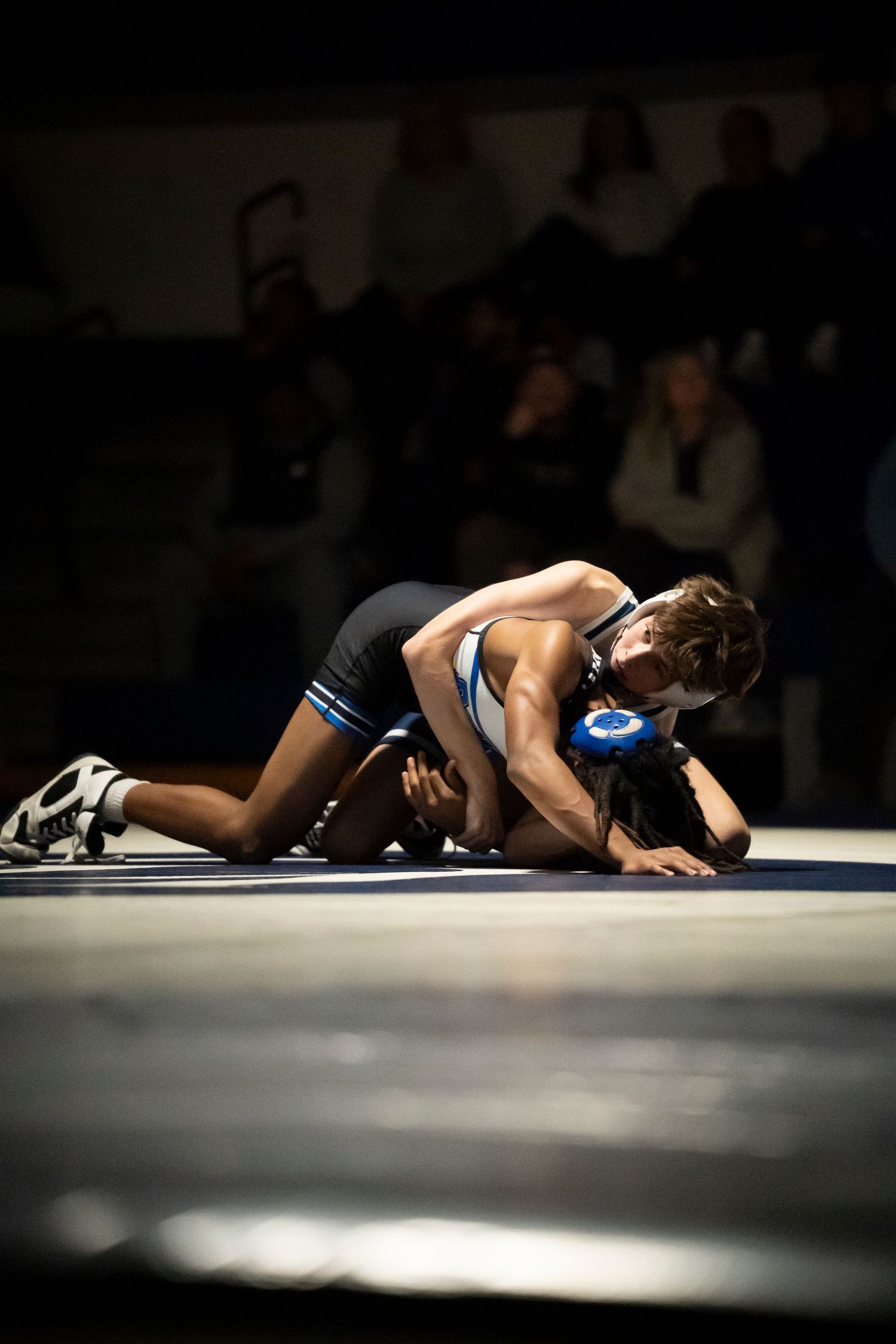 Two wrestlers compete on a mat, one pinning the other down during an indoor wrestling match.