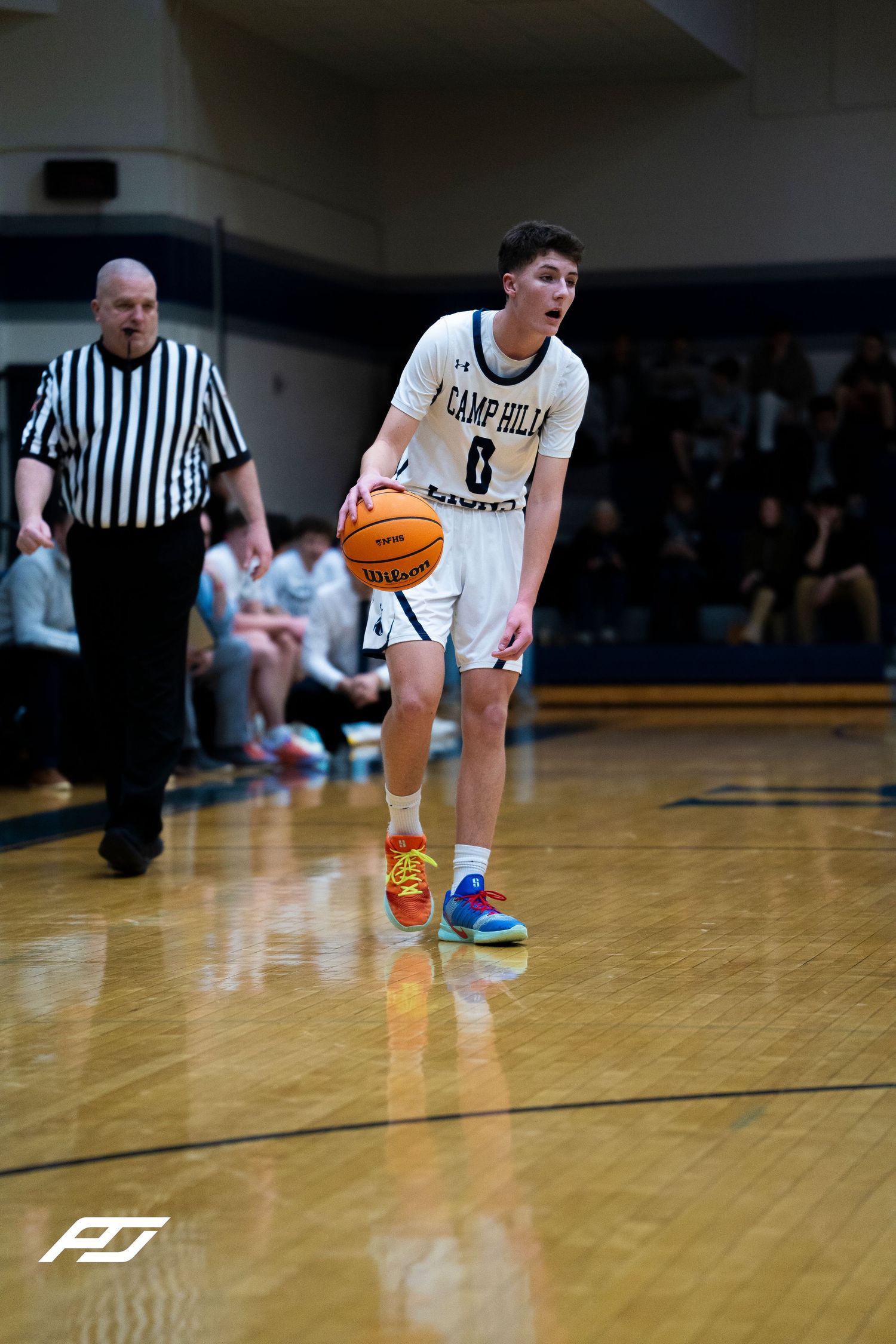 Camp Hill Lions player number 0 dribbles a basketball on a hardwood court.