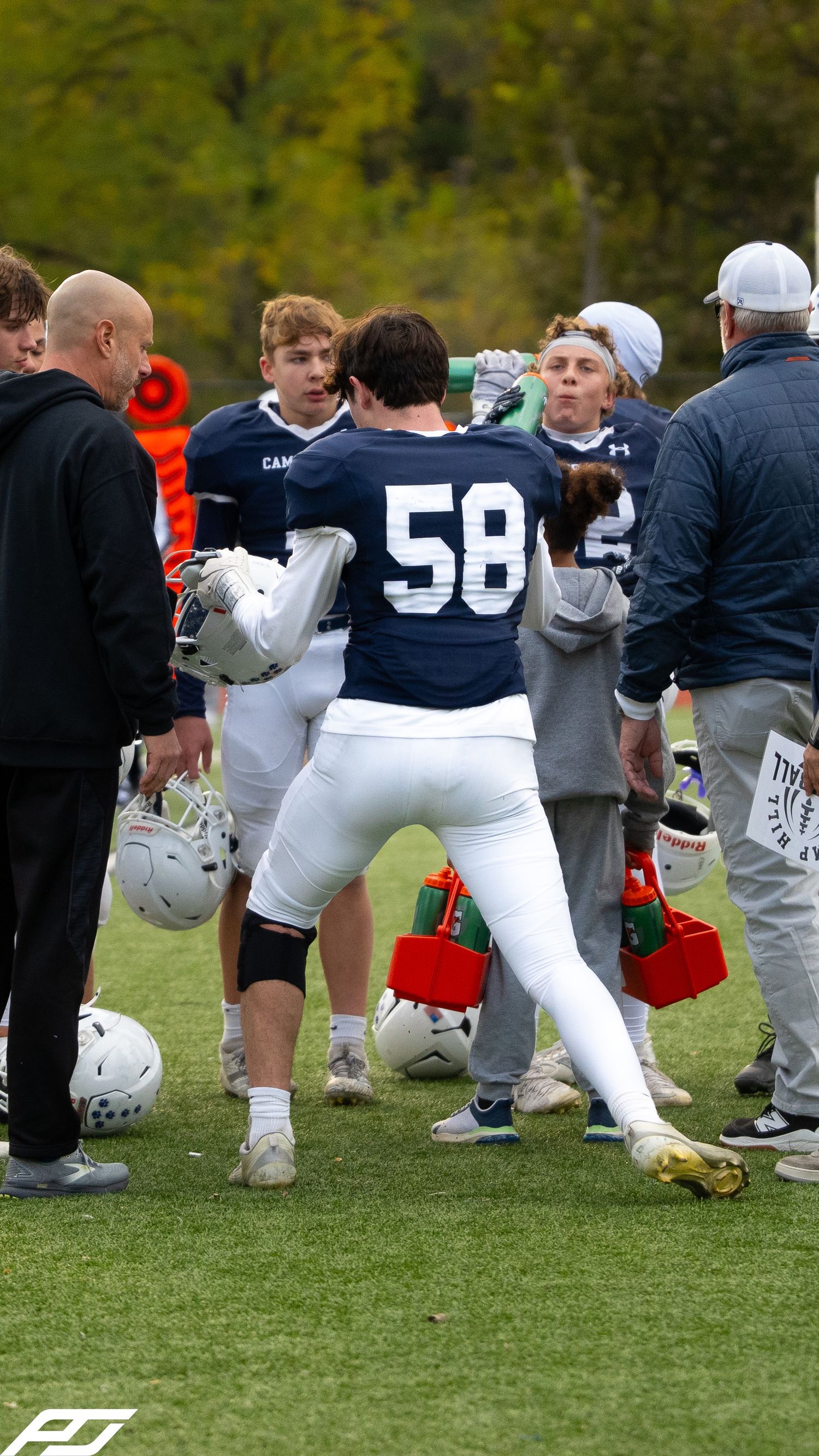 Football player number 58 in navy uniform talks with coaches and teammates.