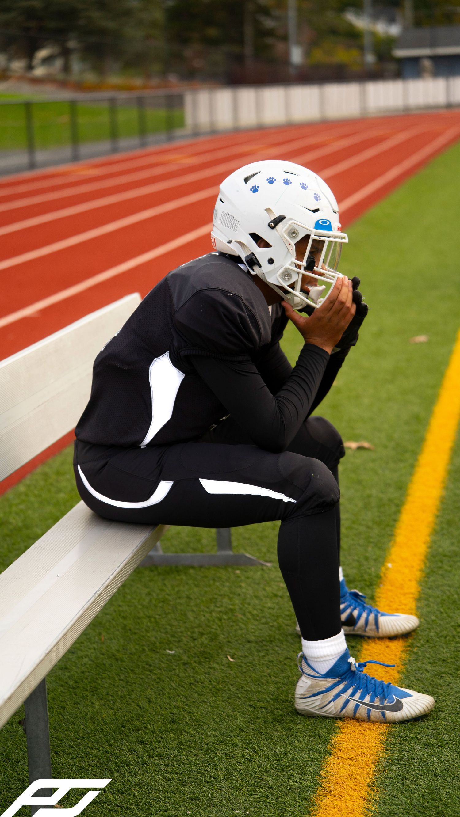 Youth football player sits on bench in full gear near a red running track.