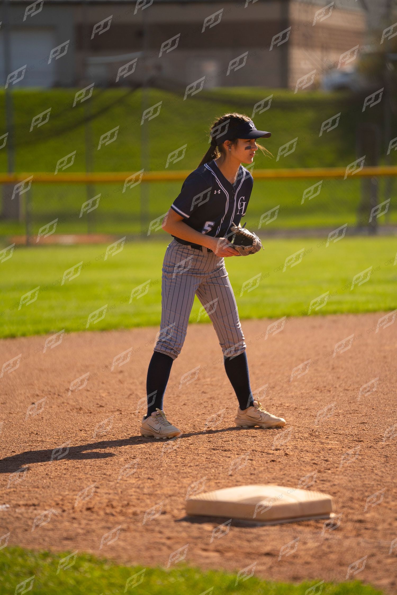 Female softball player in navy pinstripe uniform stands ready near second base during a game.