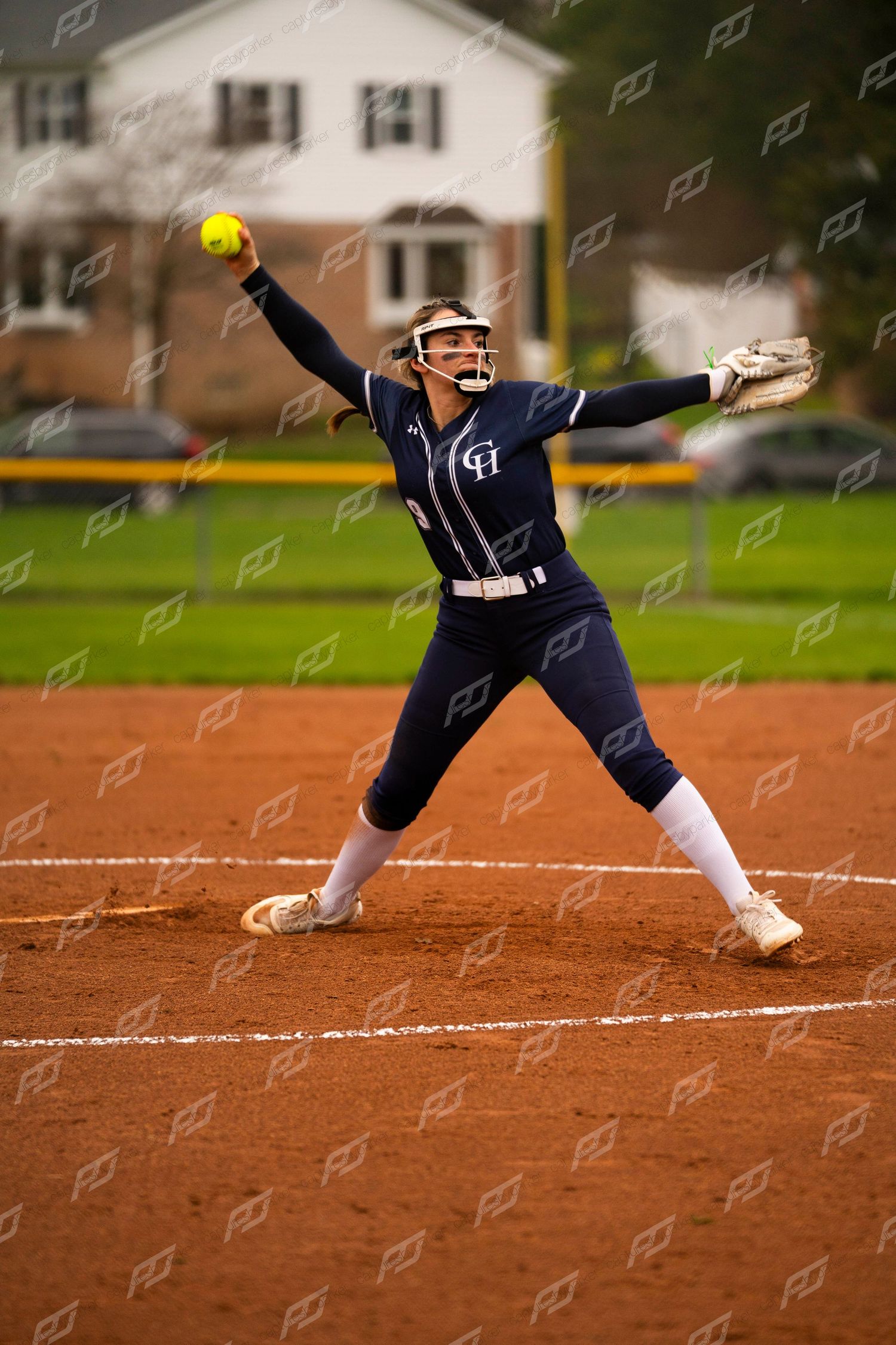 Female softball pitcher in navy CH uniform delivers a windmill pitch during game.