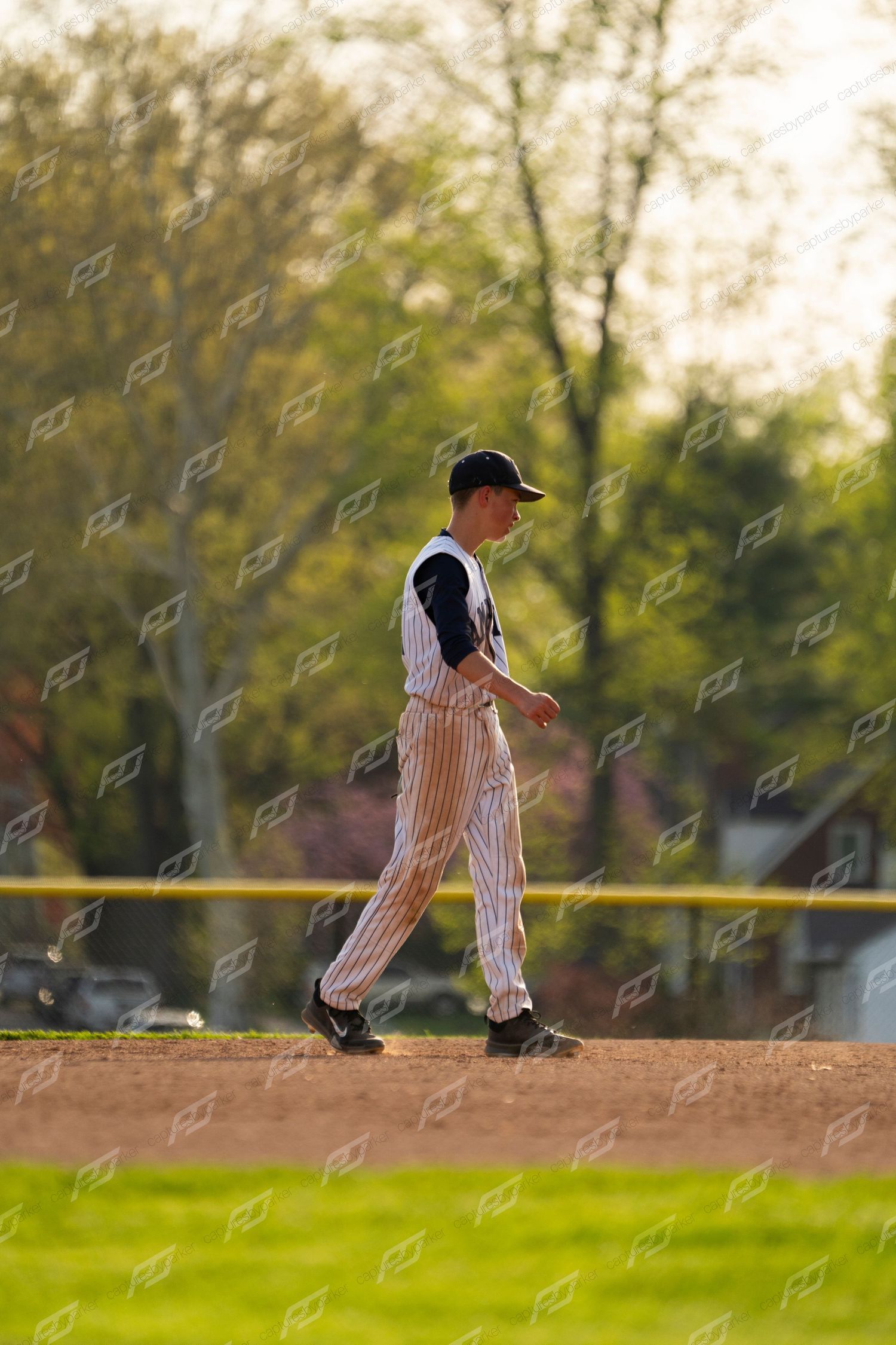 Baseball player in pinstripe uniform walking on the infield dirt during a game on a sunny day.