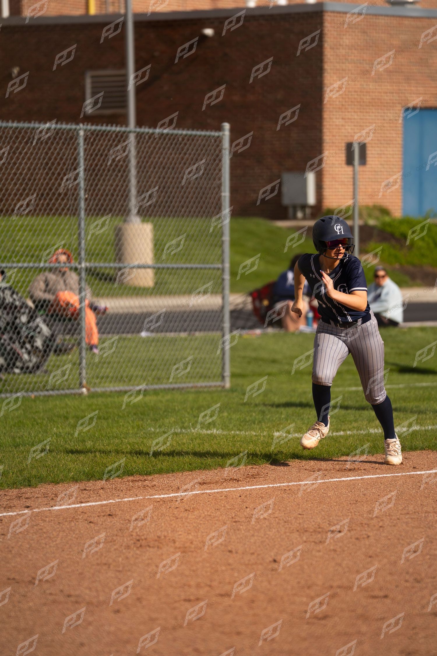 Female softball player in navy uniform takes a lead off base during a softball game.