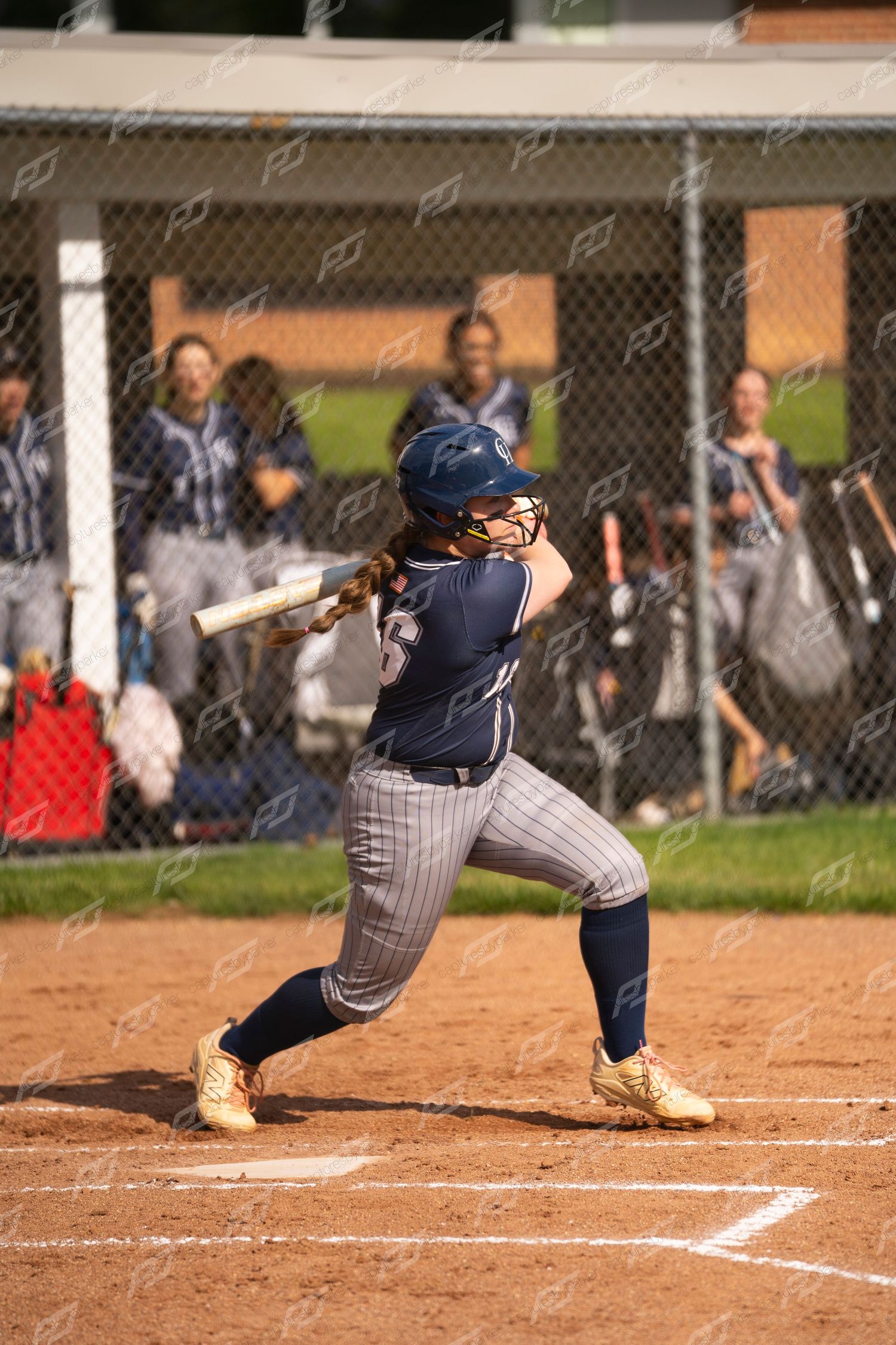 Female softball player in navy uniform follows through on swing during outdoor game.