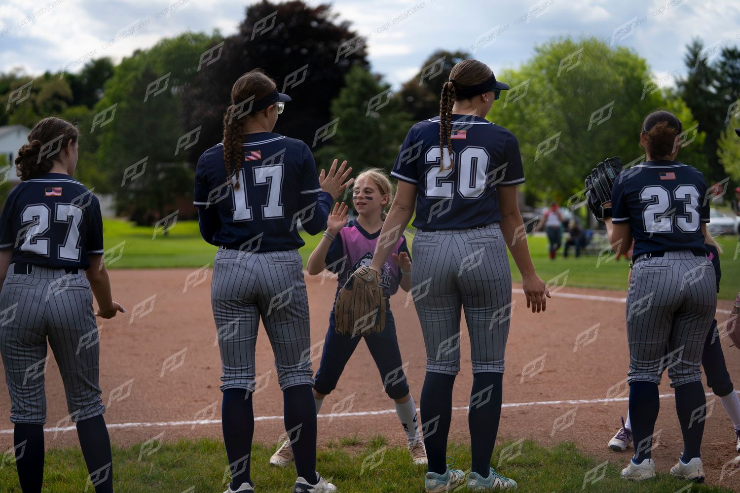 Softball players in navy pinstripe uniforms exchange high-fives with a young child on the field.