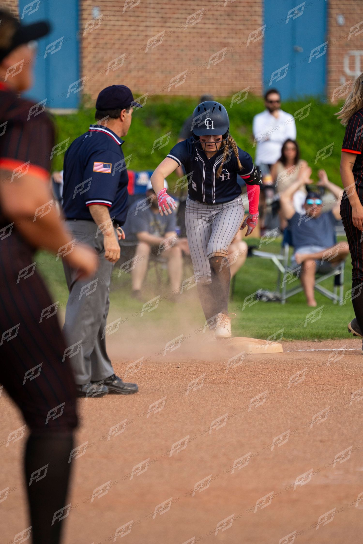 Female softball player slides into base in cloud of dust near umpire.