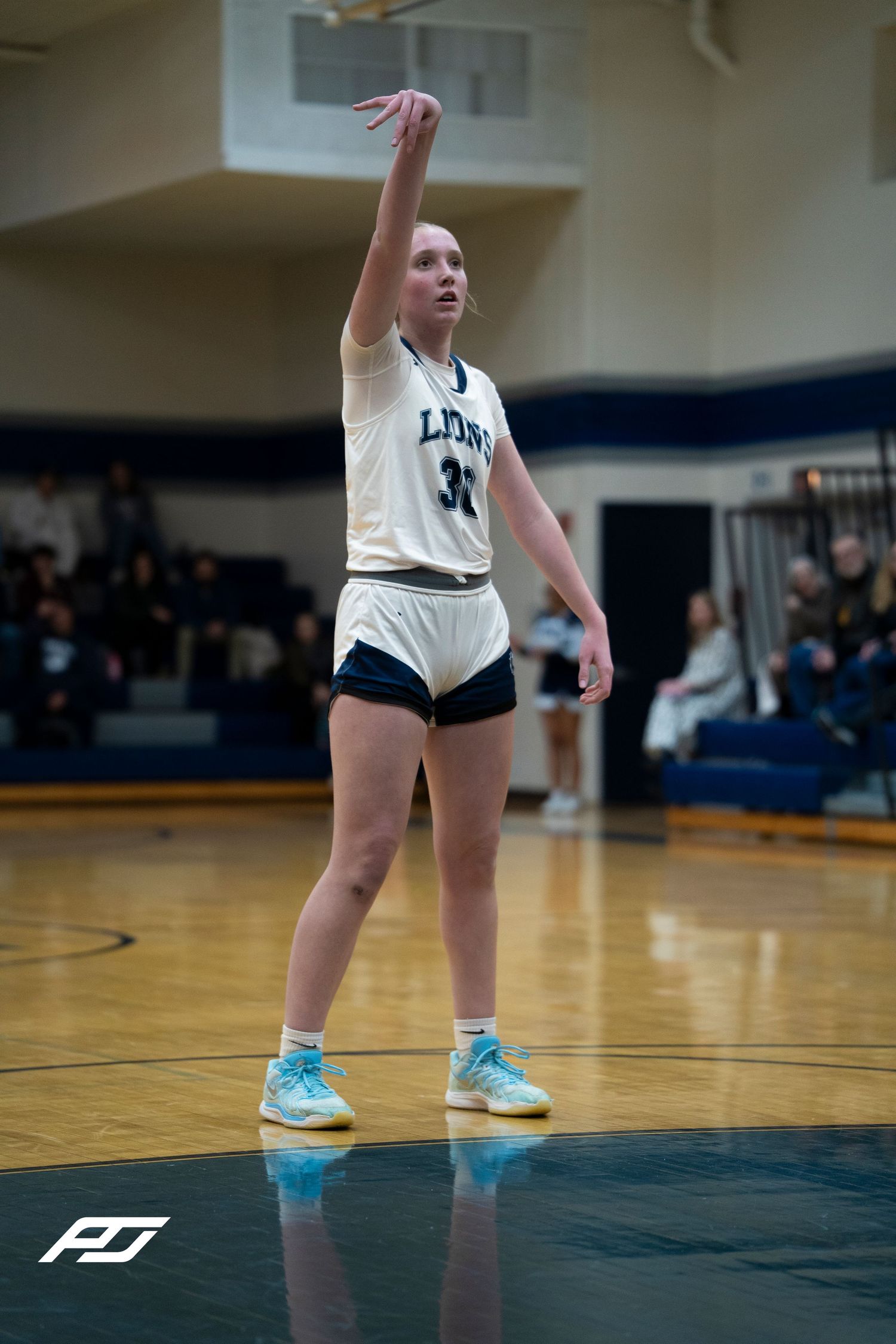 Lions #31 female basketball player follows through on jump shot during high school game.