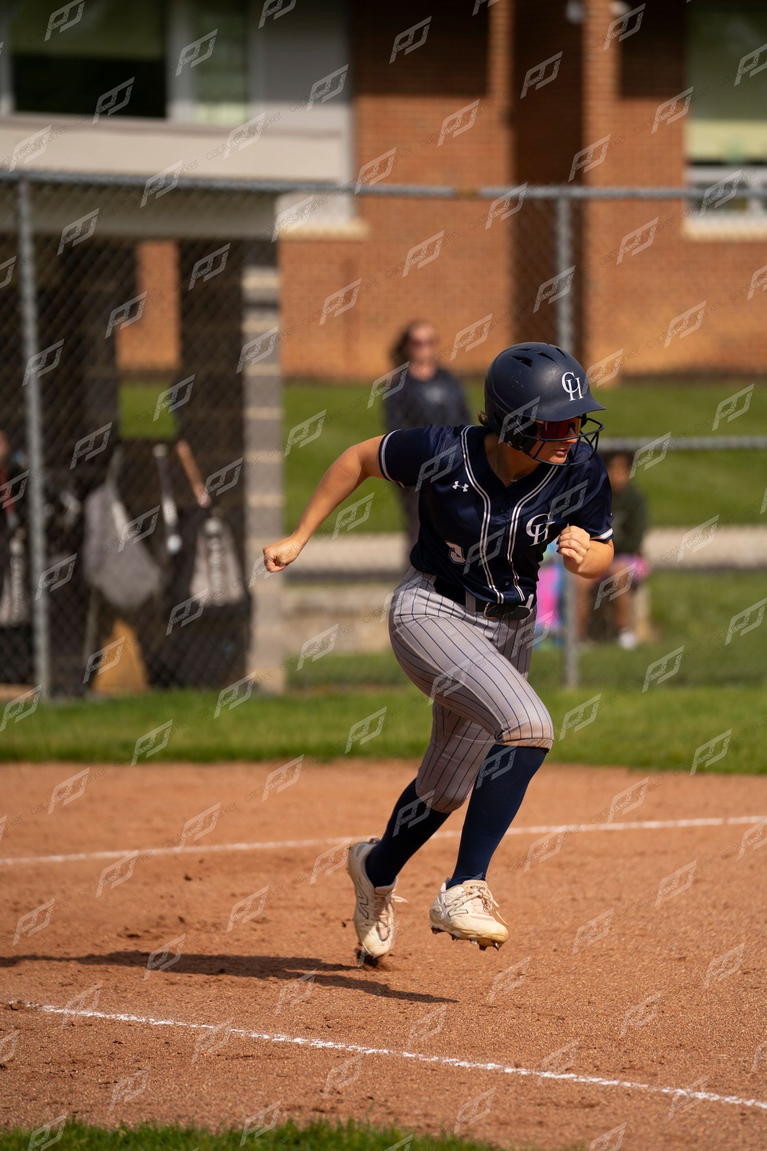 Softball player in navy pinstripe uniform runs bases during game.