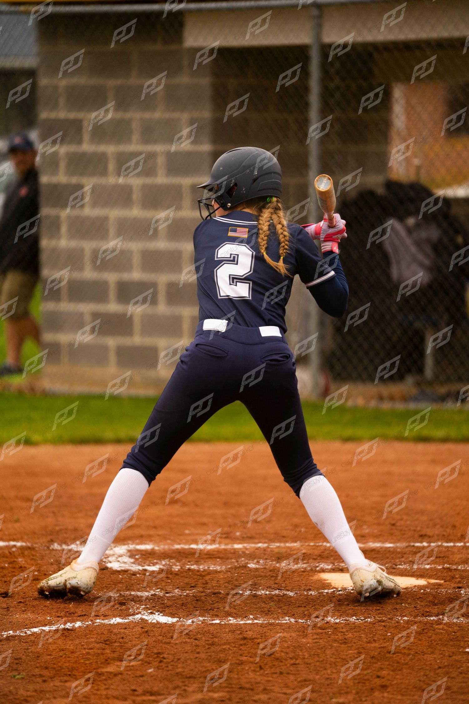 Female softball player #2 in navy uniform stands in batting stance ready to hit.