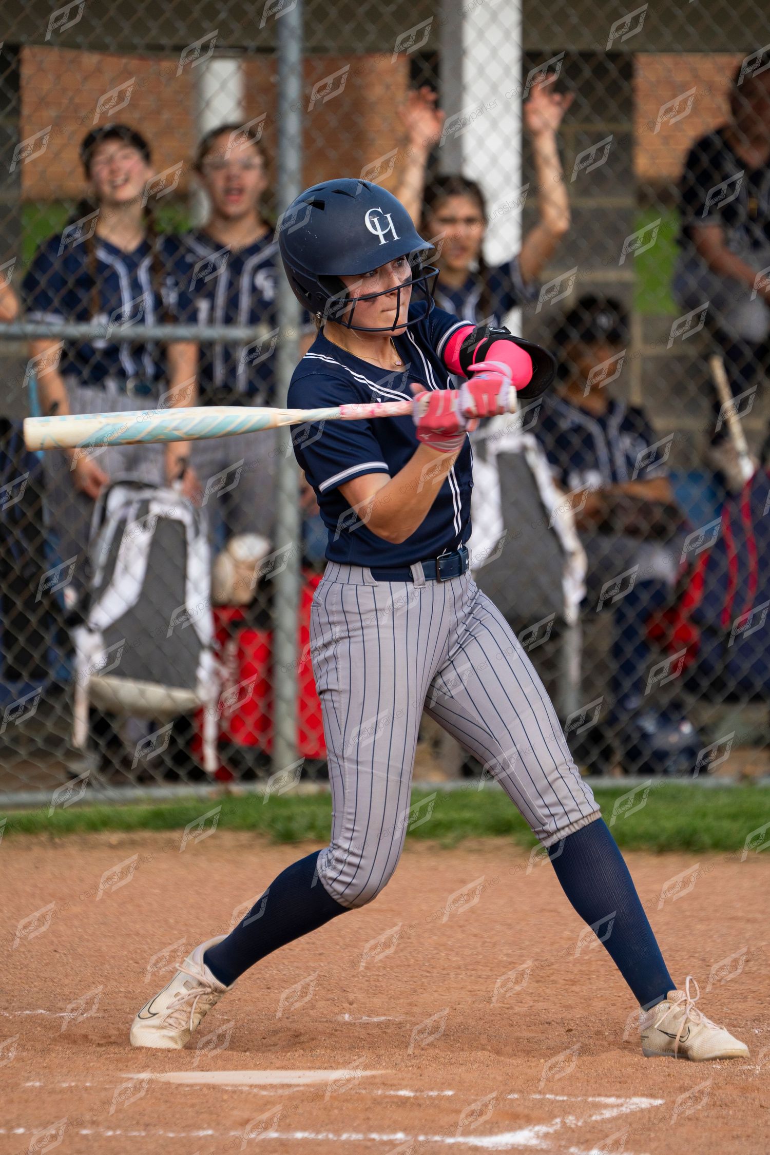 Female softball player in navy pinstripe uniform swings bat during game.