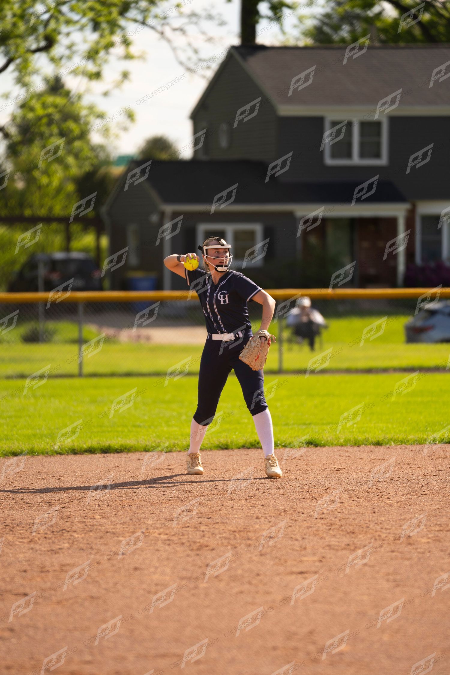 Female softball player in navy uniform preparing to throw the ball from the infield dirt.
