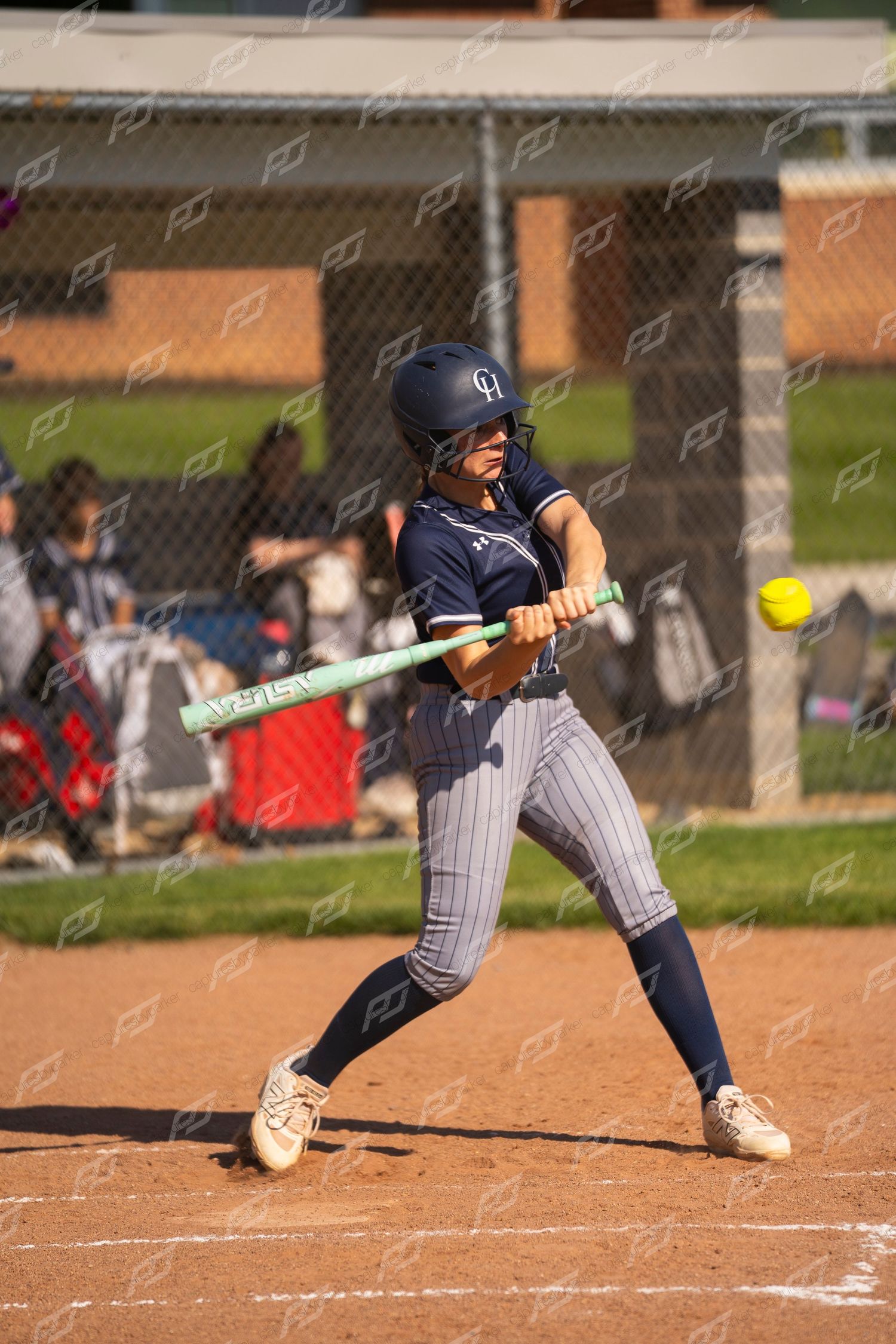 Female softball batter makes contact with a yellow ball during a sunny outdoor game.