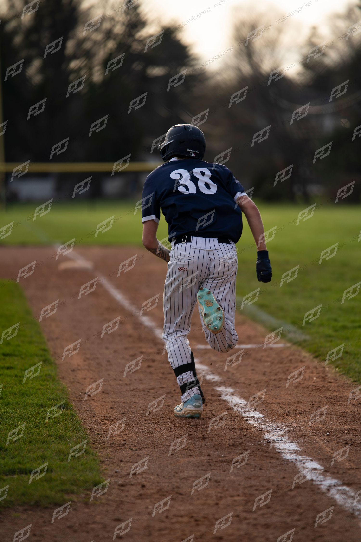Baseball player #38 runs down the baseline during an outdoor game at dusk.