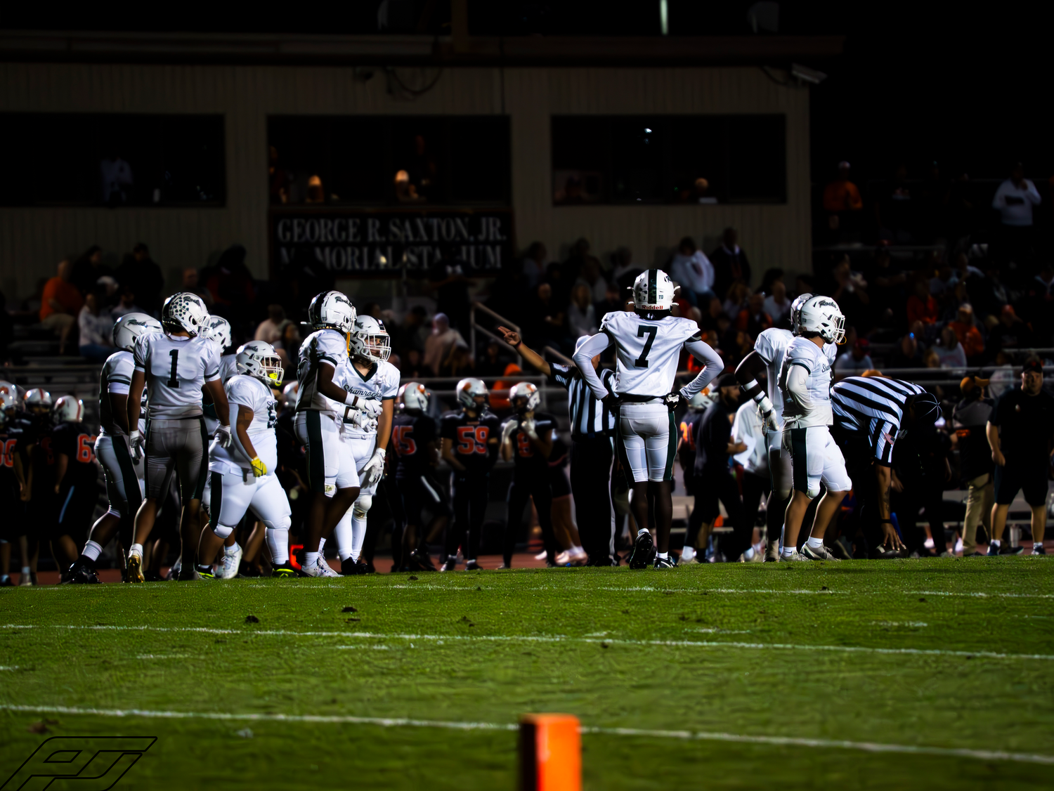 High school football team huddles near end zone during night game.