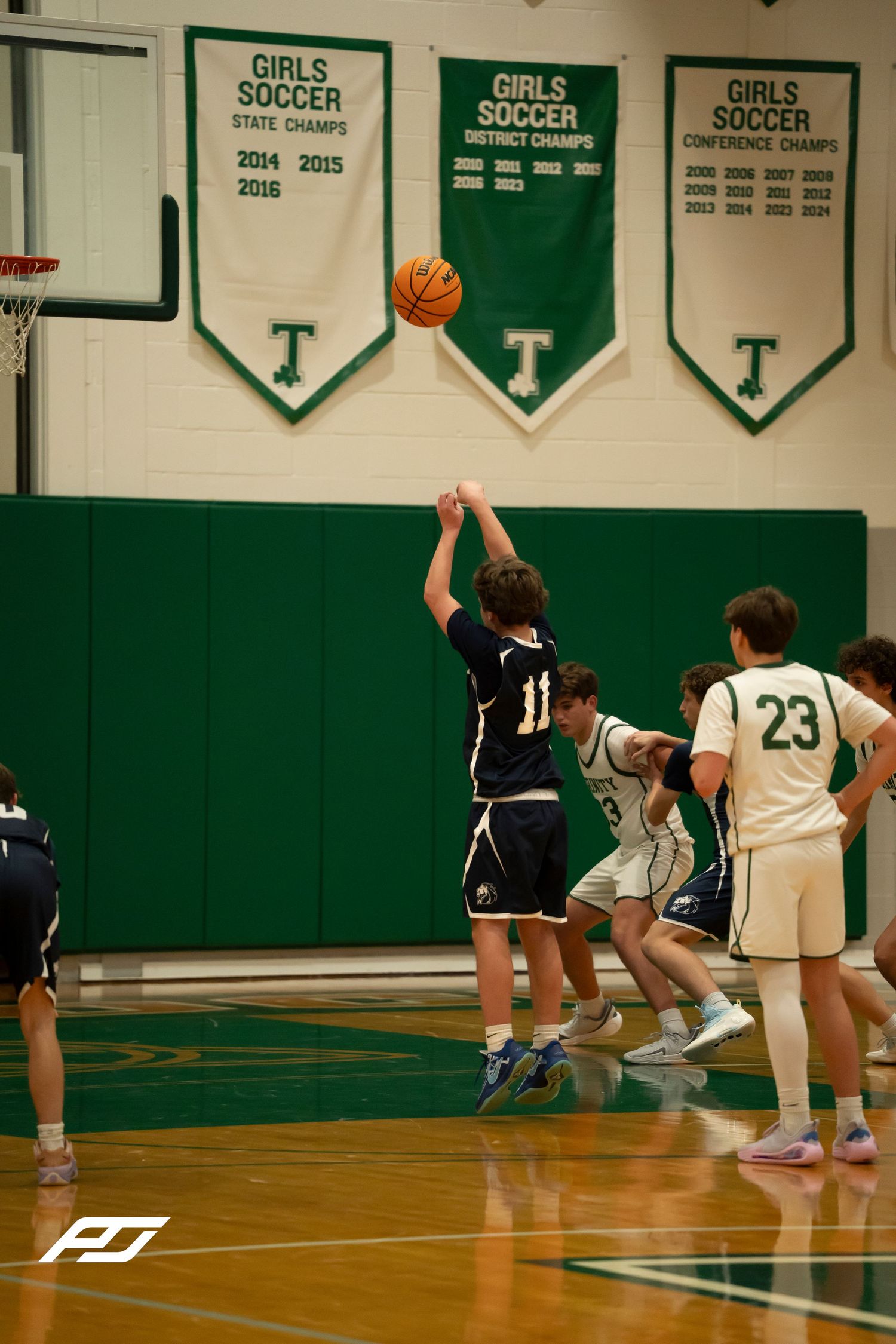 Number 11 basketball player in navy uniform releases a jump shot during a high school basketball game.