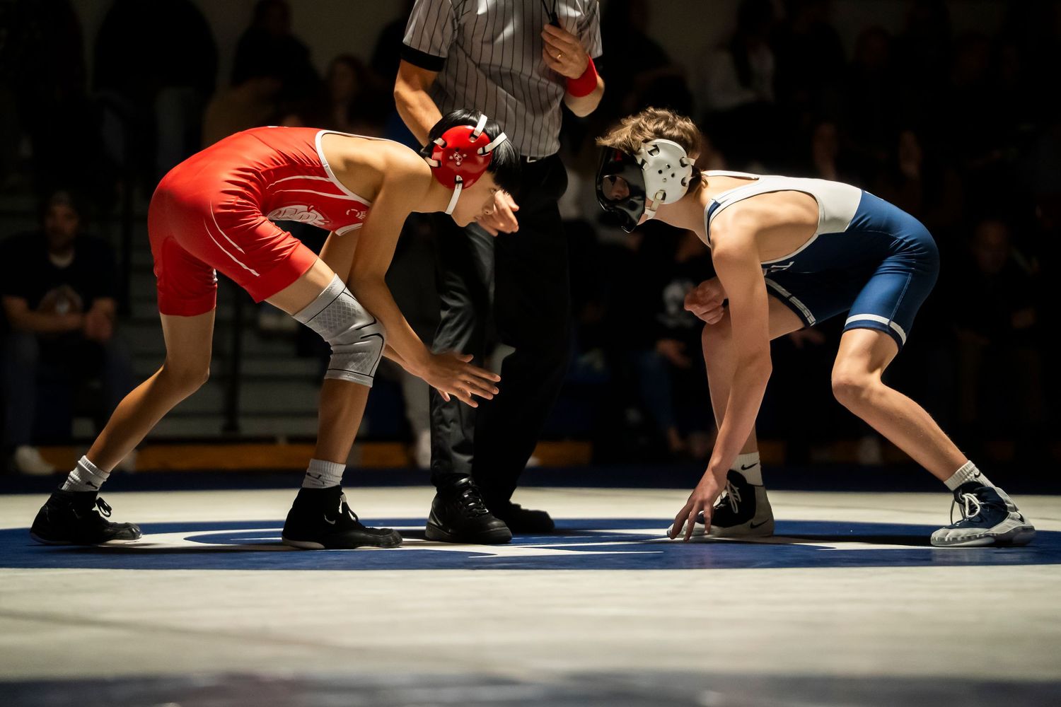 Two high school wrestlers face off in red and blue singlets before a wrestling match.