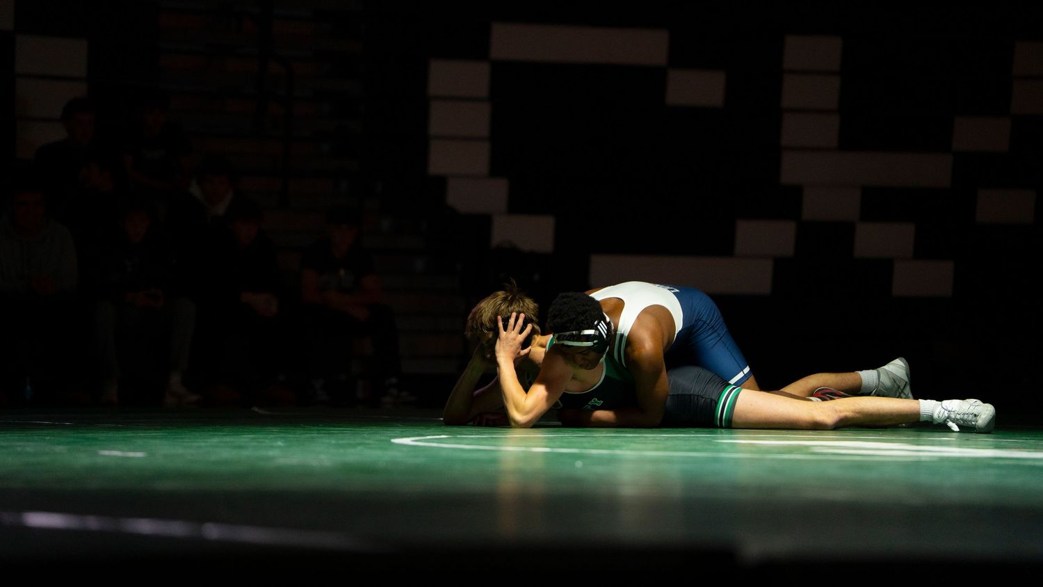 Wrestler in blue singlet pins opponent flat on green mat during a competitive wrestling match.