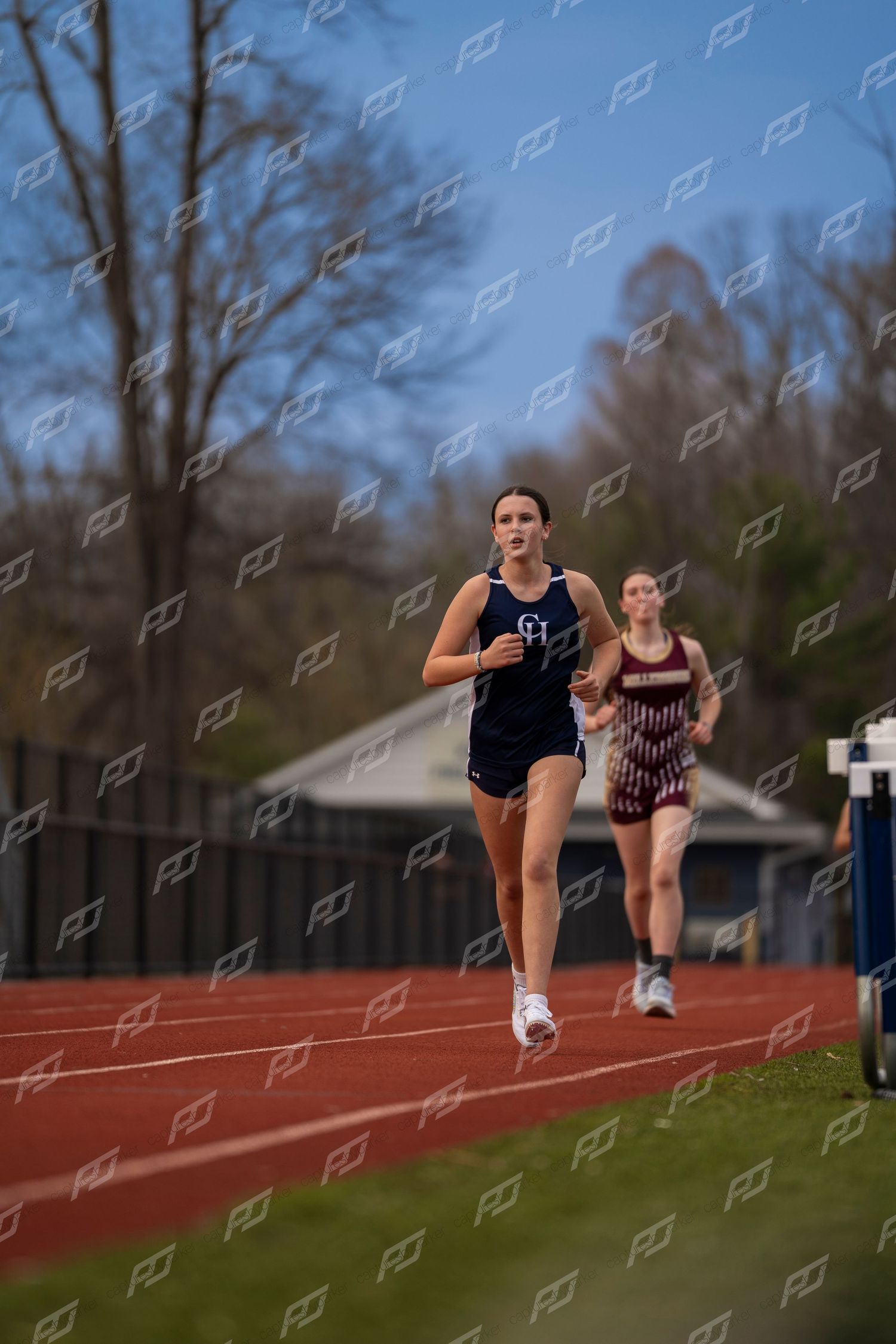 Female track athlete in navy CH uniform leading race on outdoor red track.