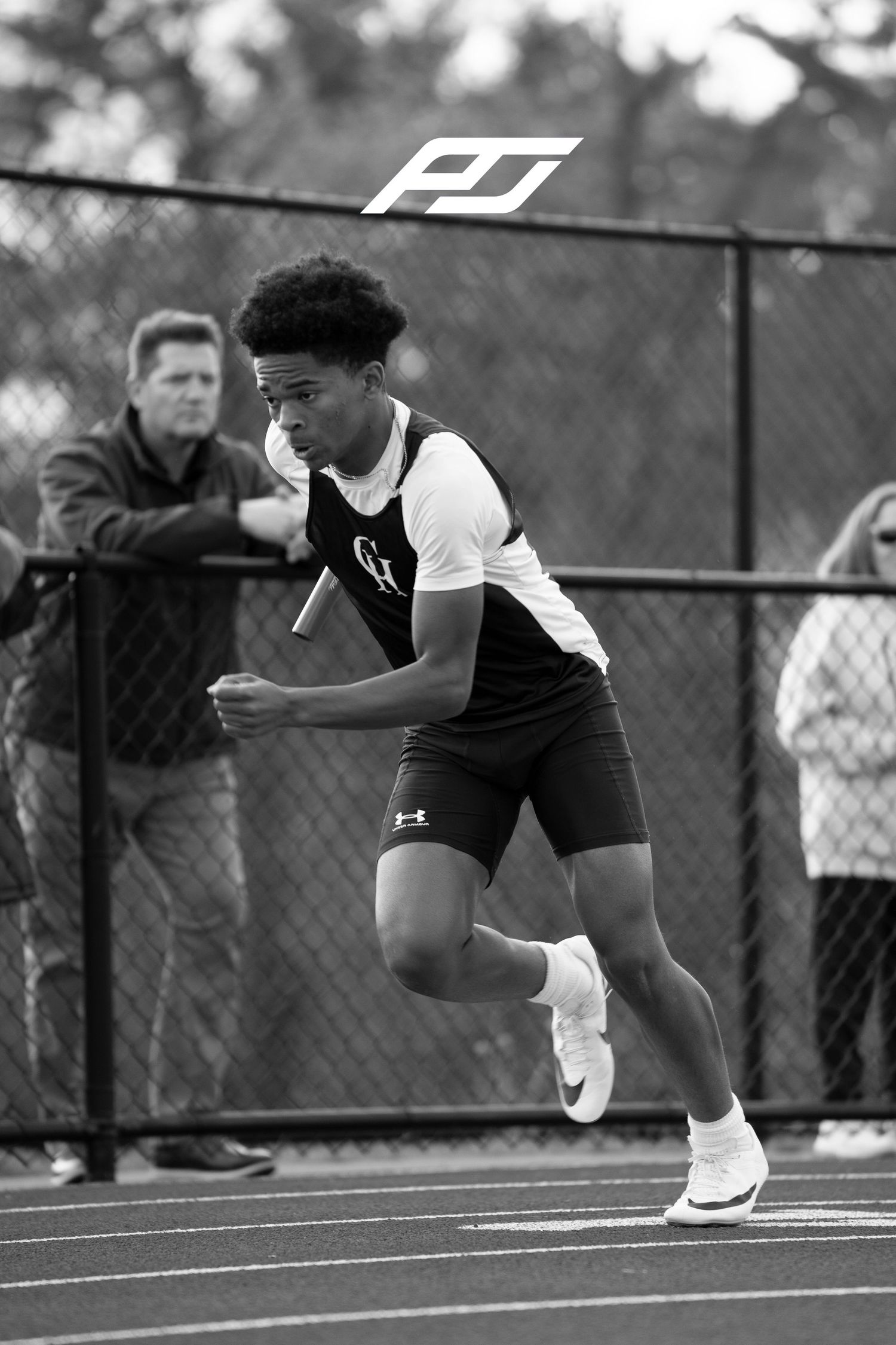 High school sprinter in GH uniform accelerates during outdoor relay race carrying baton.