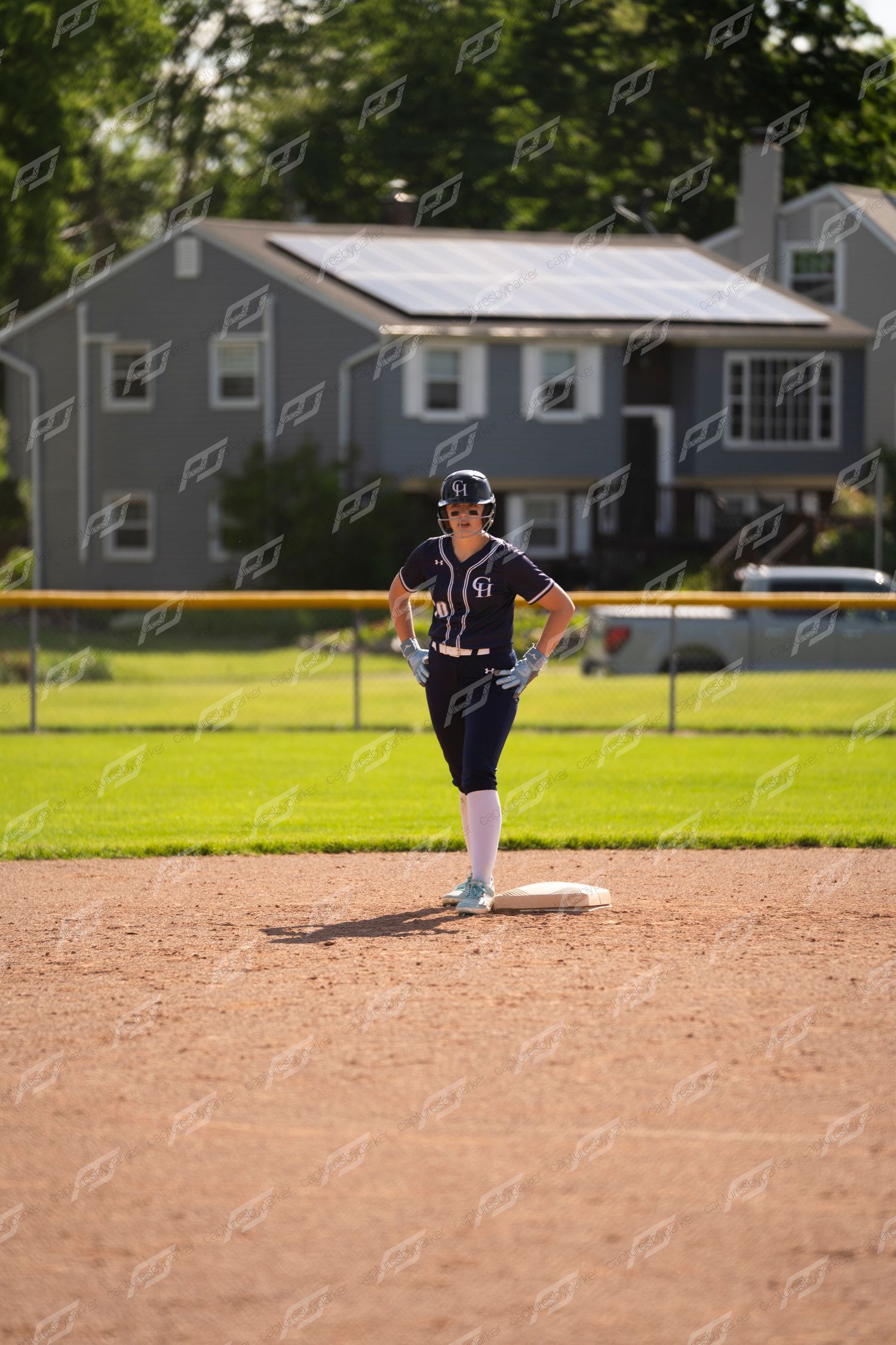 Softball player in navy uniform stands on second base with hands on hips during a game.