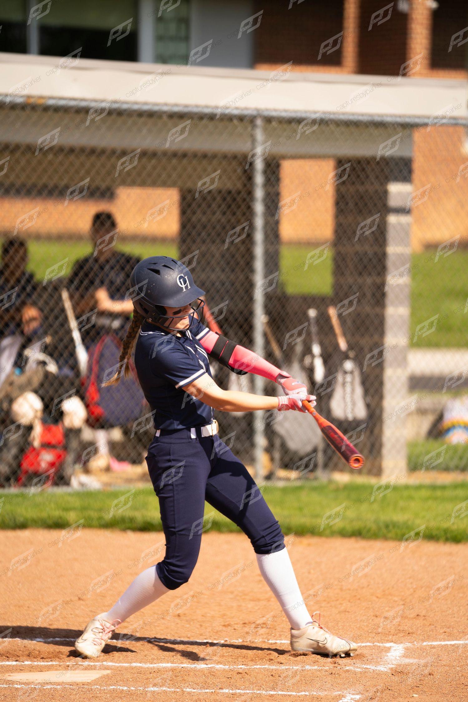Female softball batter in navy uniform swings red bat at pitch during game.