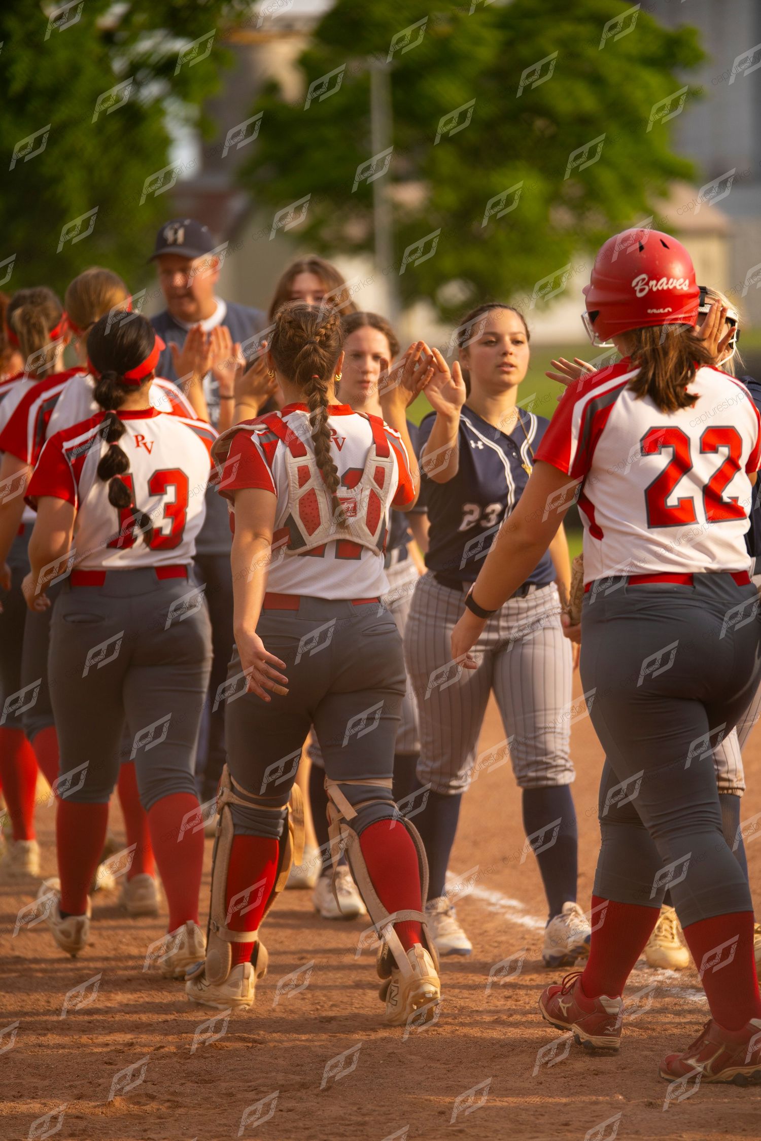 Red and navy team softball players celebrate with high fives near home plate.