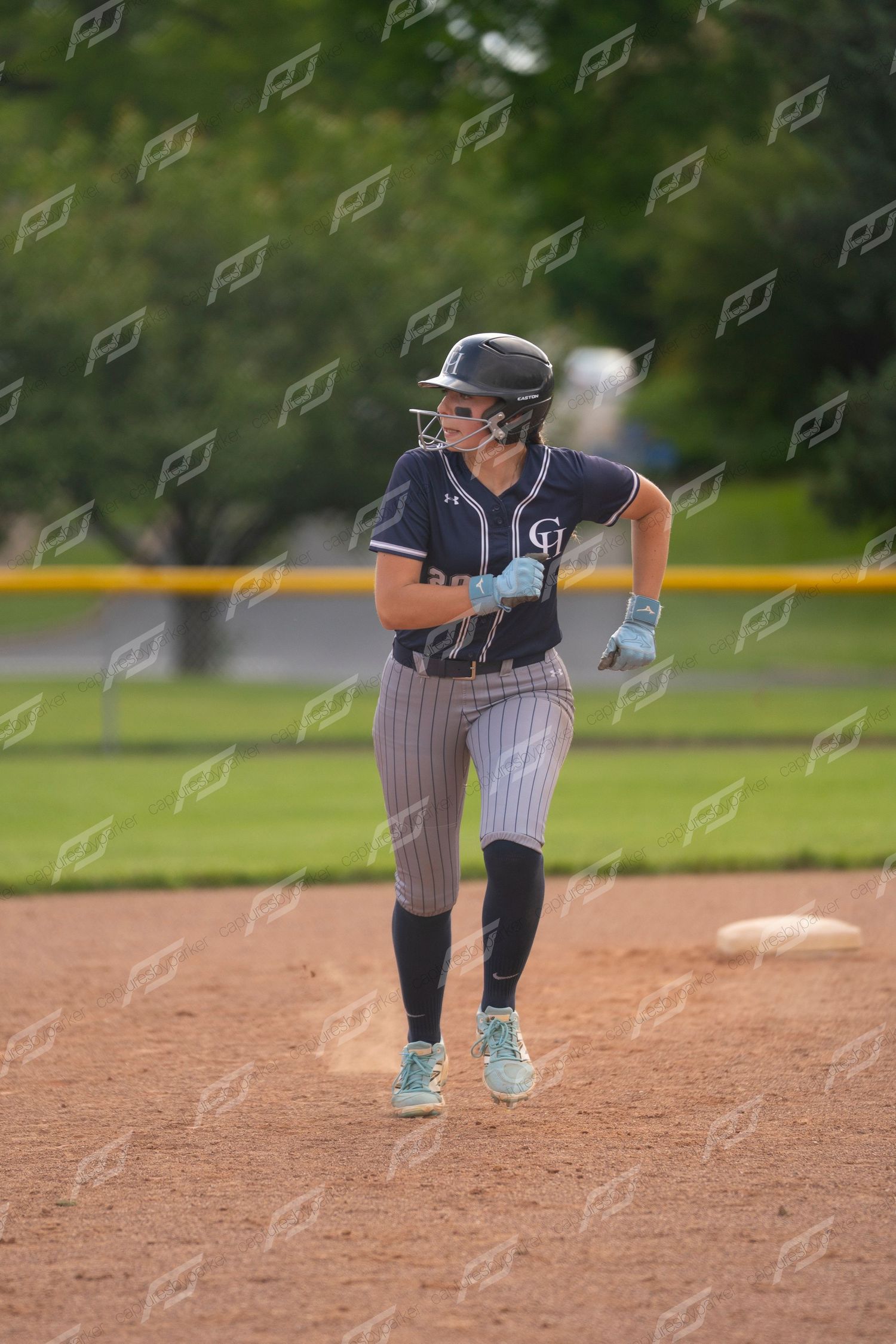 Softball player in navy uniform rounding second base during an outdoor game.