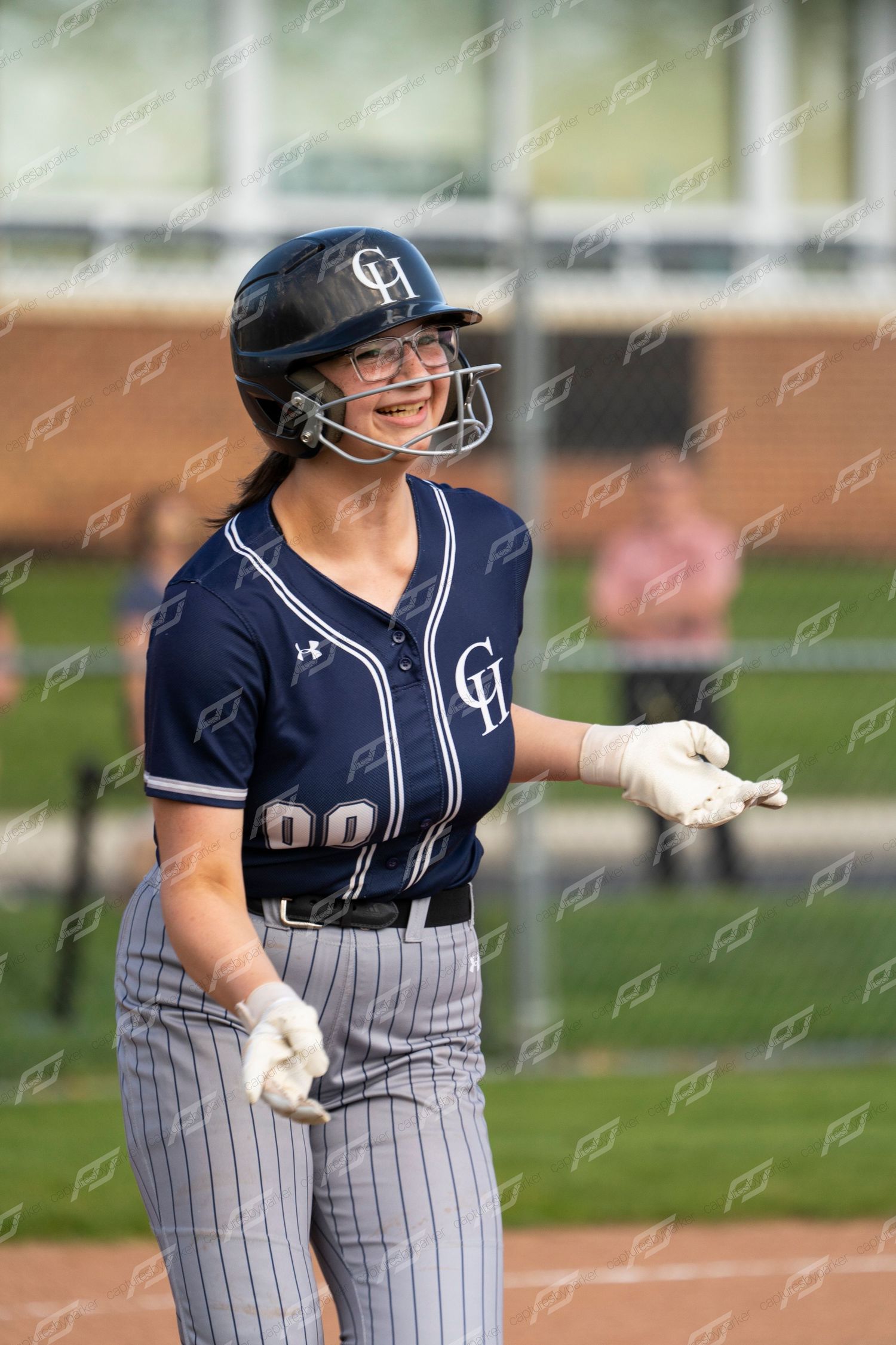 Smiling female CH softball player in navy uniform and helmet stands on base during a game.