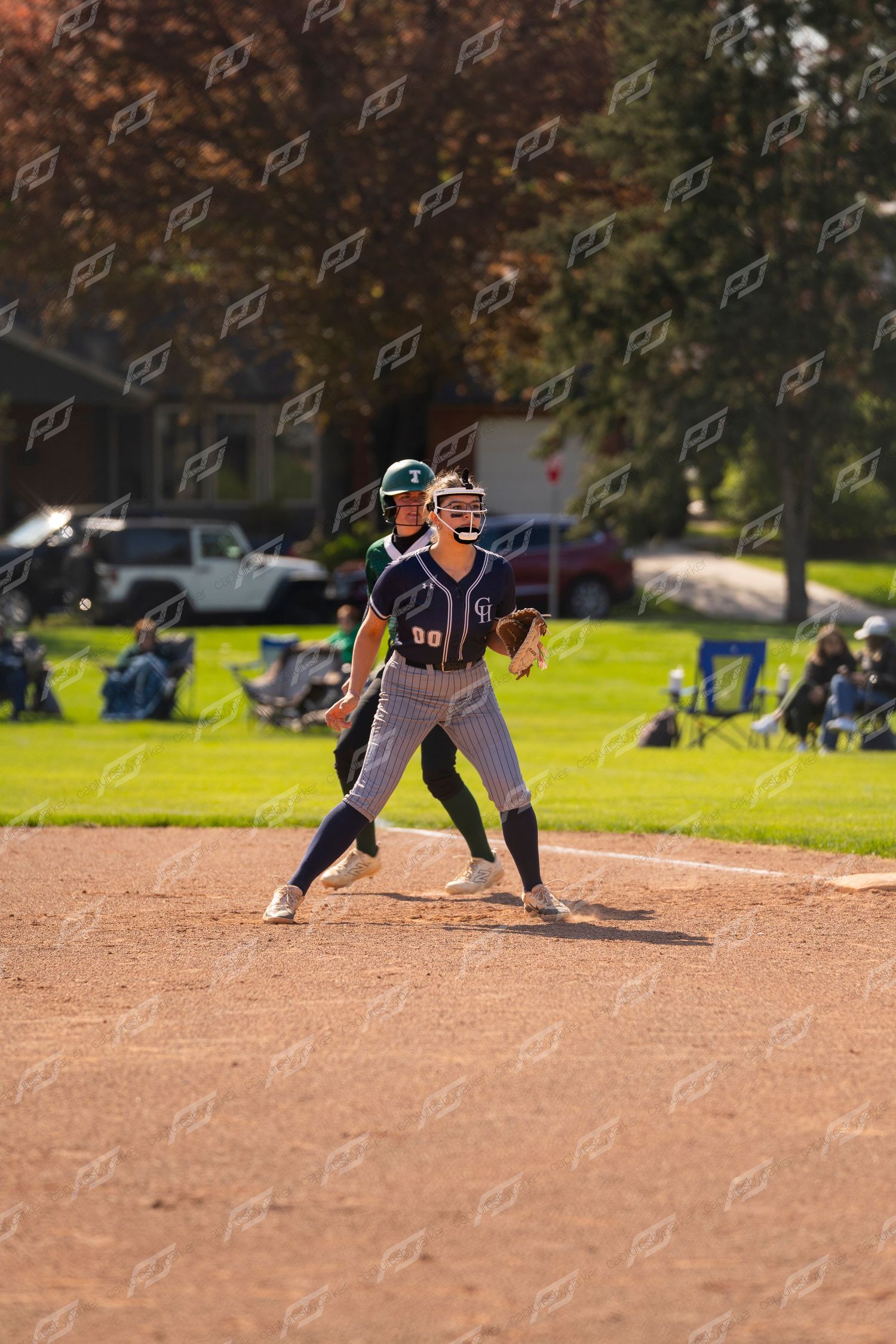 Female softball player #00 in navy pinstripe uniform fields ball at third base during game.