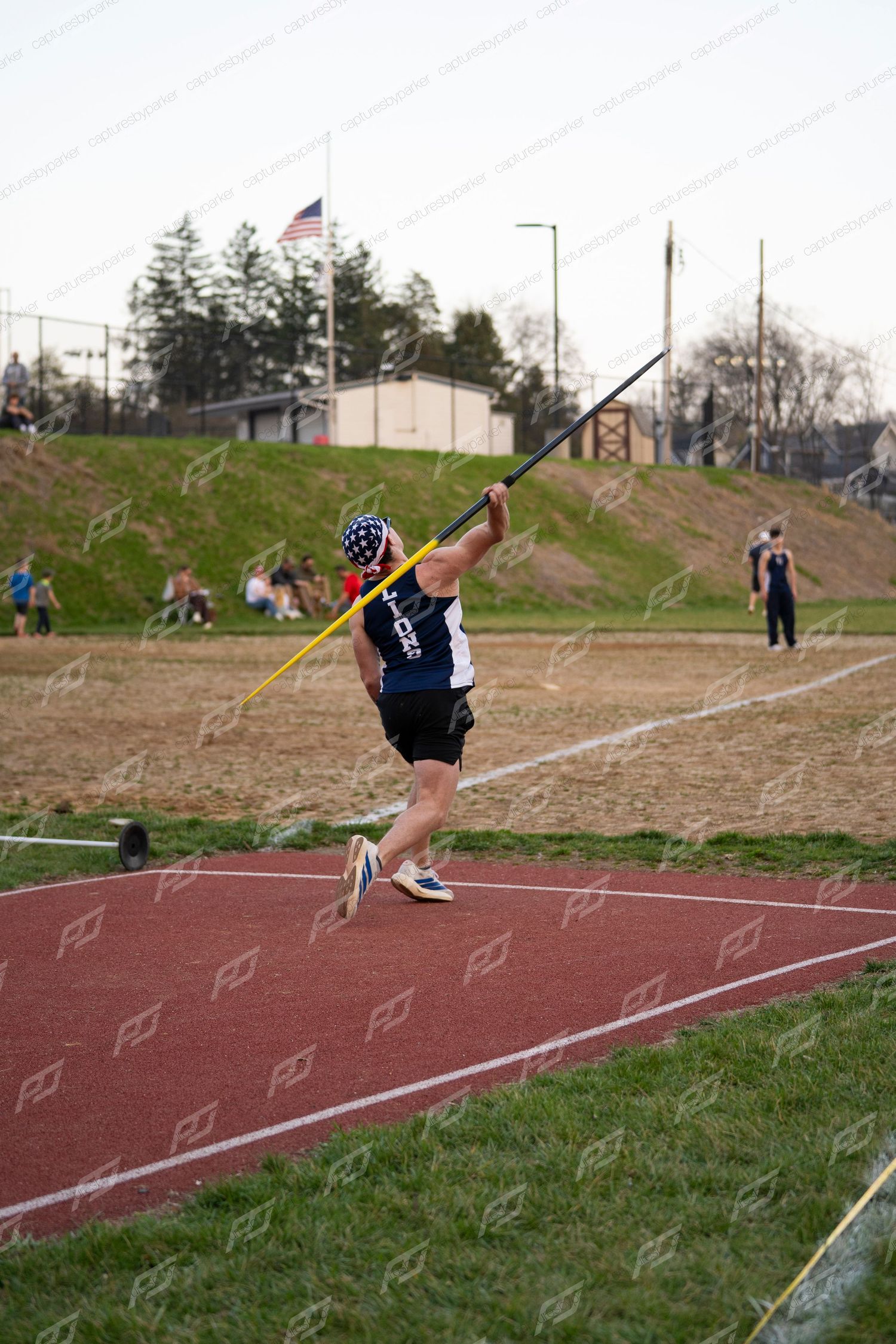 Male athlete prepares to release javelin during outdoor track and field competition at dusk.